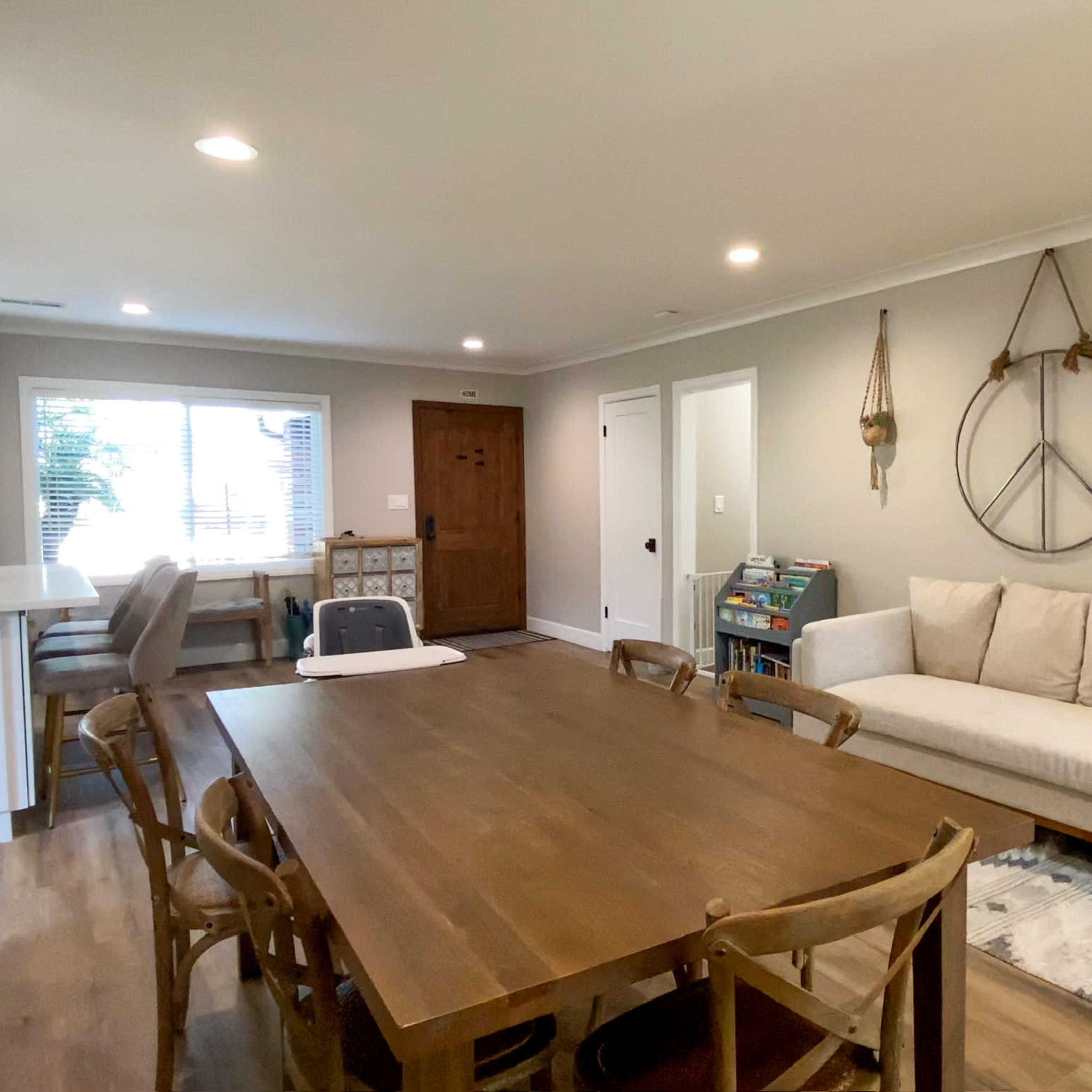 A well-lit dining area with a wooden table, chairs, and a cozy couch alongside a window and a door leading outside.
