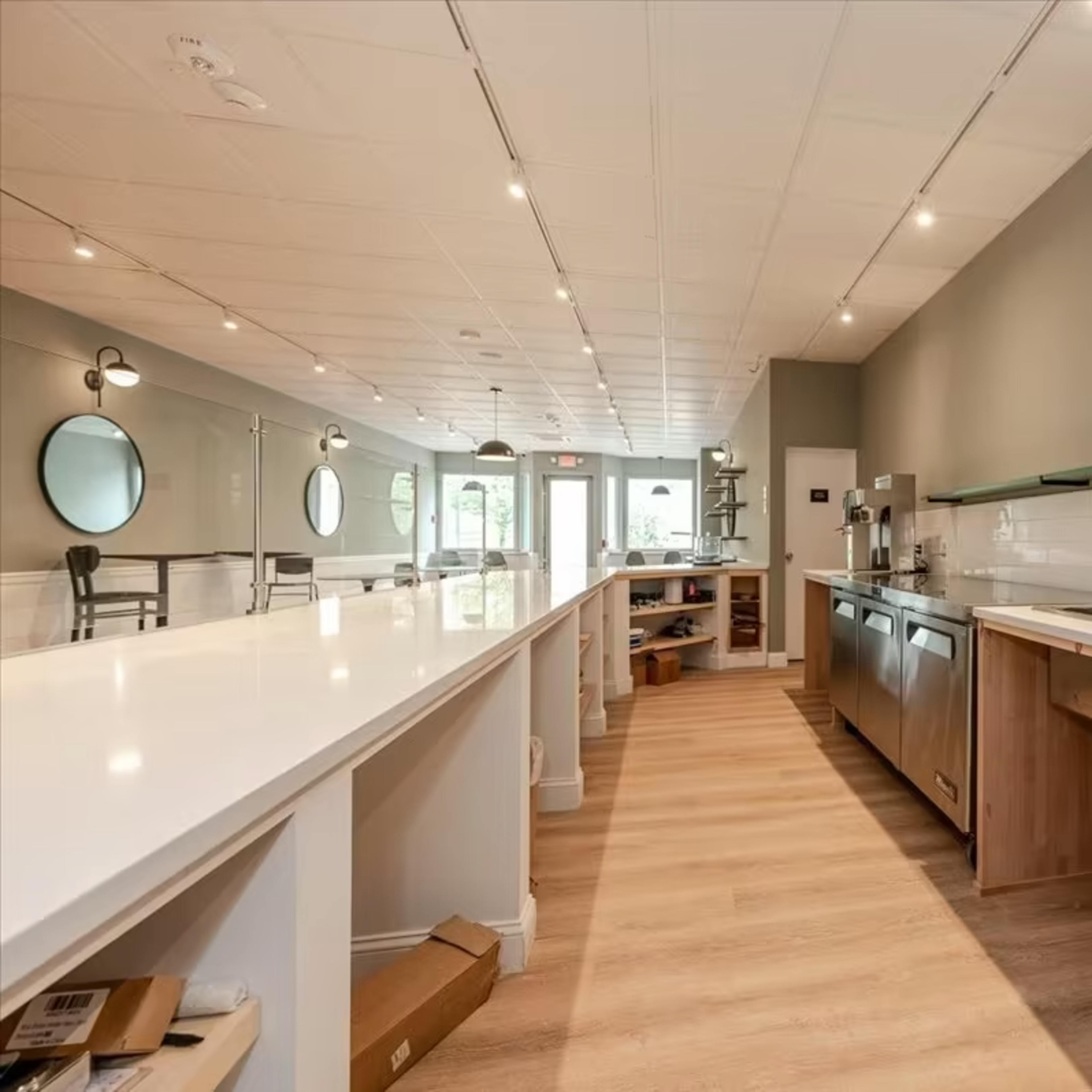 A modern, empty kitchen space with a long, white countertop, stainless steel appliances, and wooden cabinetry.