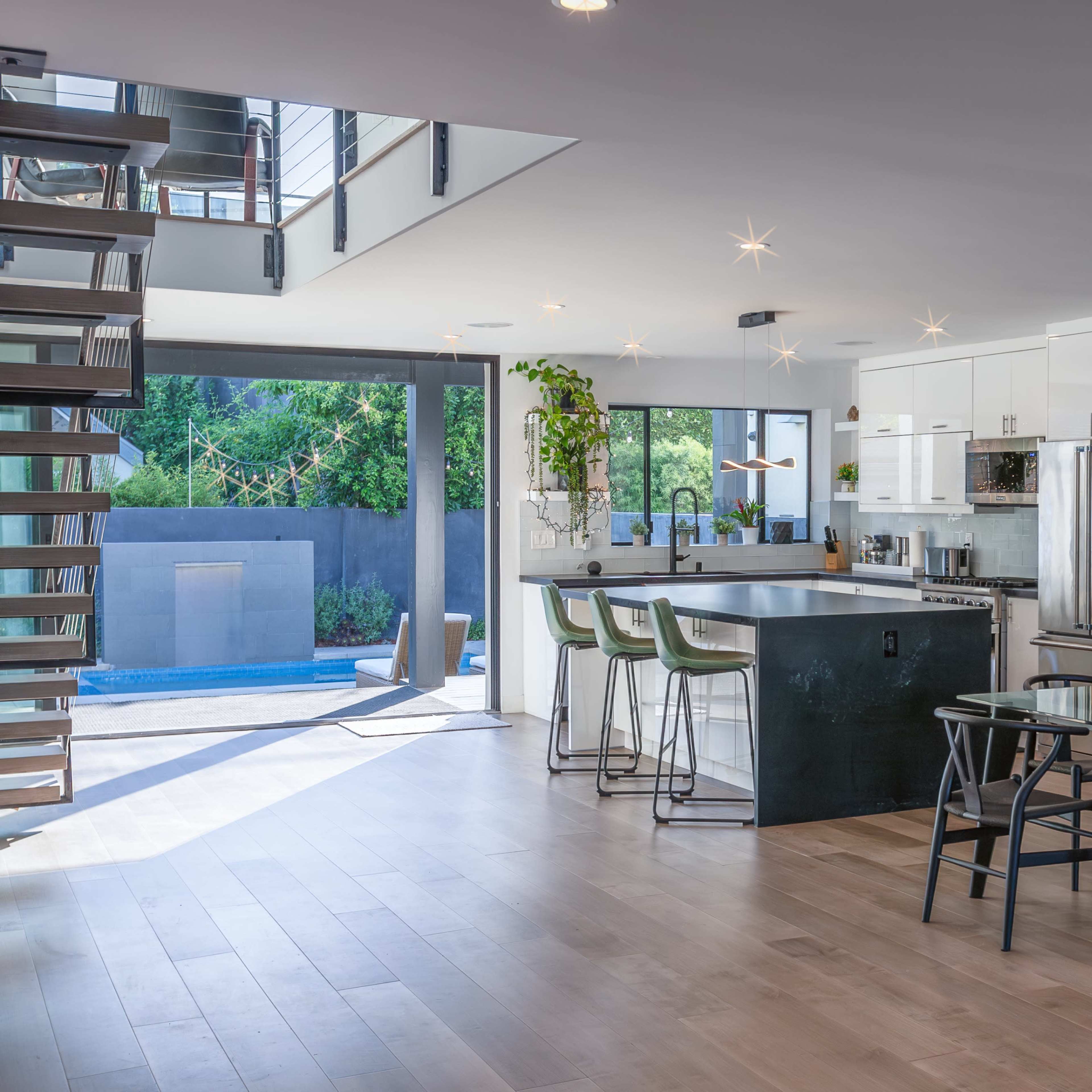 A modern open-plan kitchen and dining area, featuring a large island, sleek cabinetry, and a dining table with black chairs, all illuminated by bright ceiling lights.
