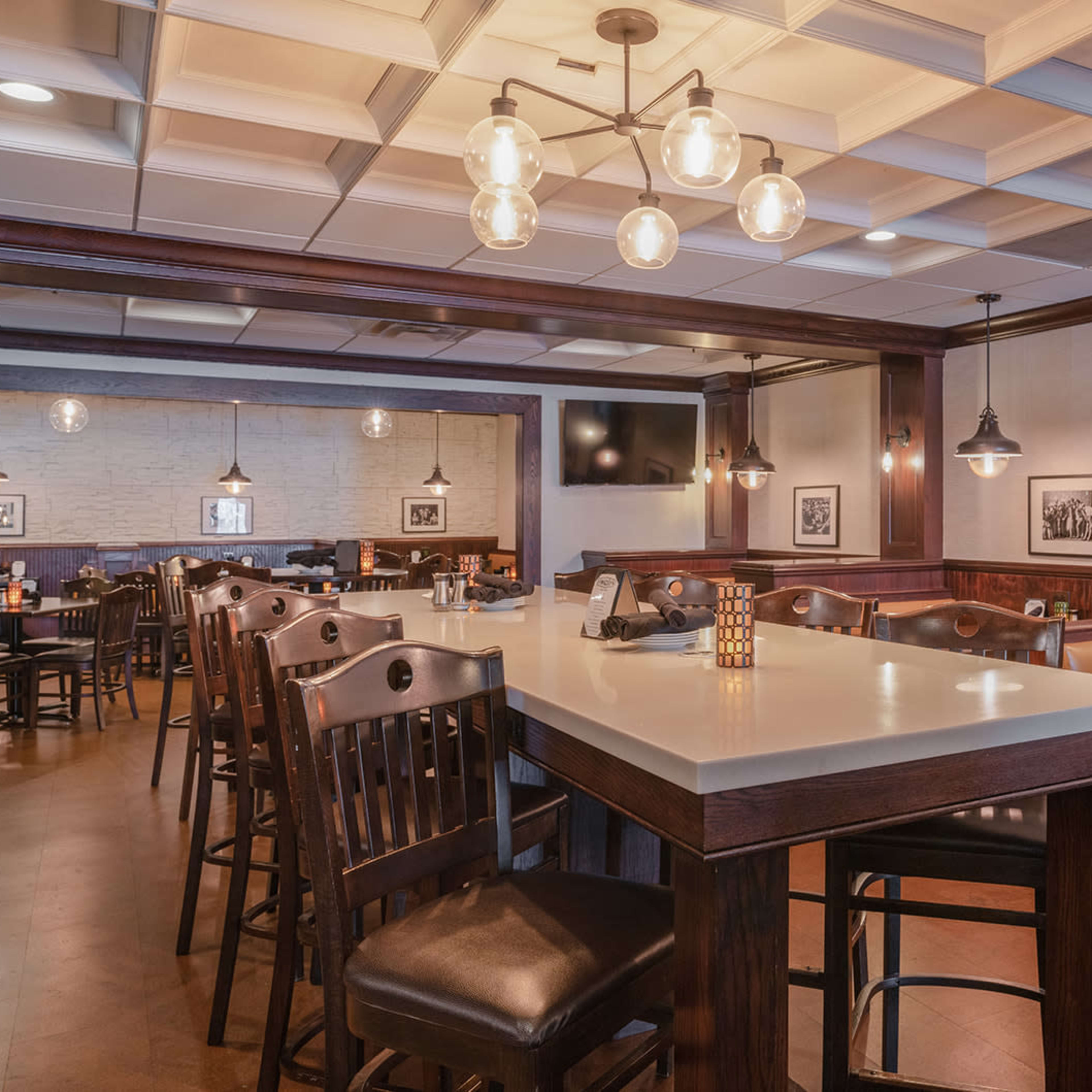 A modern restaurant interior with wooden furniture, dim lighting, and a long bar counter.