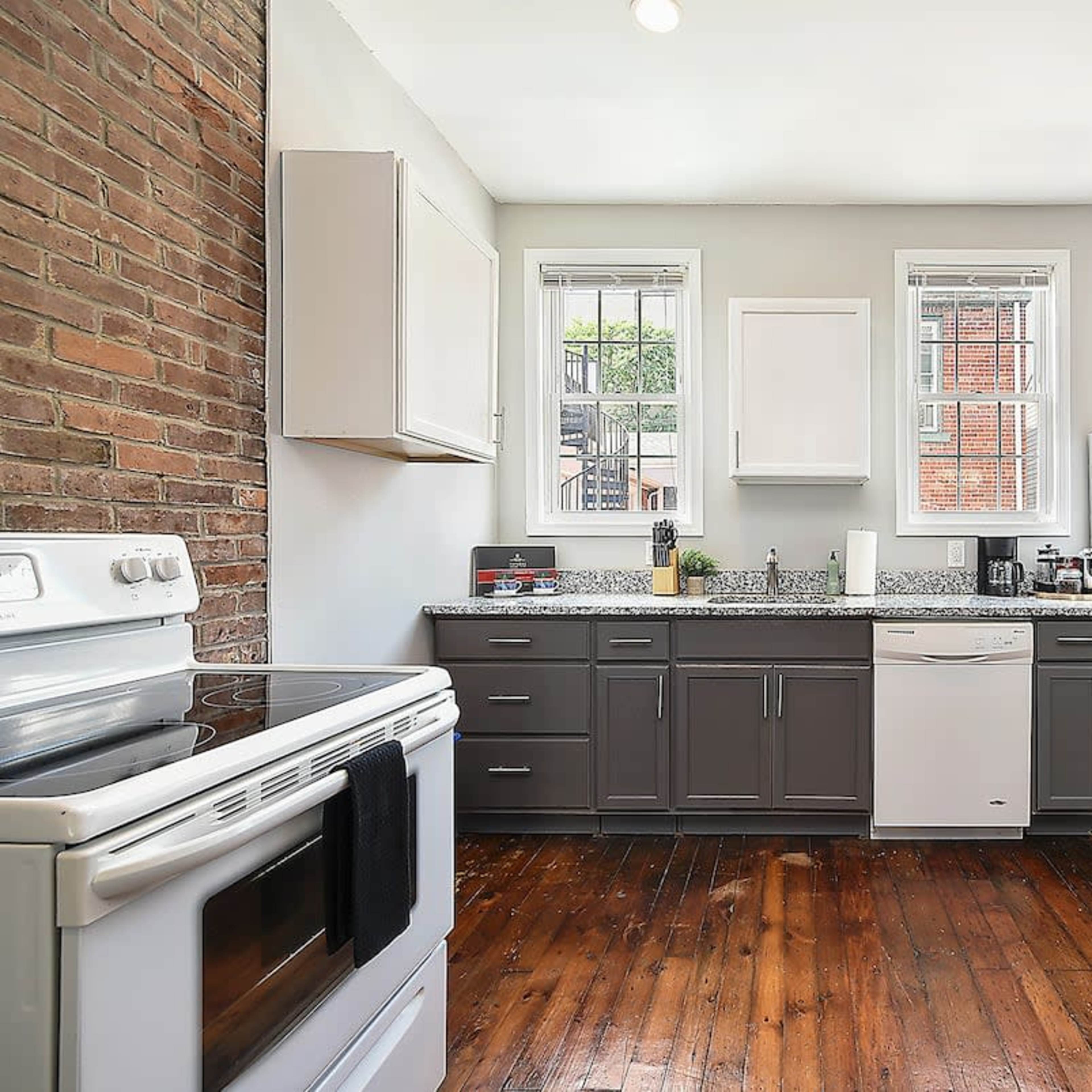 The kitchen features a combination of brick and painted walls, with a stove, refrigerator, and dishwasher arranged along a countertop.