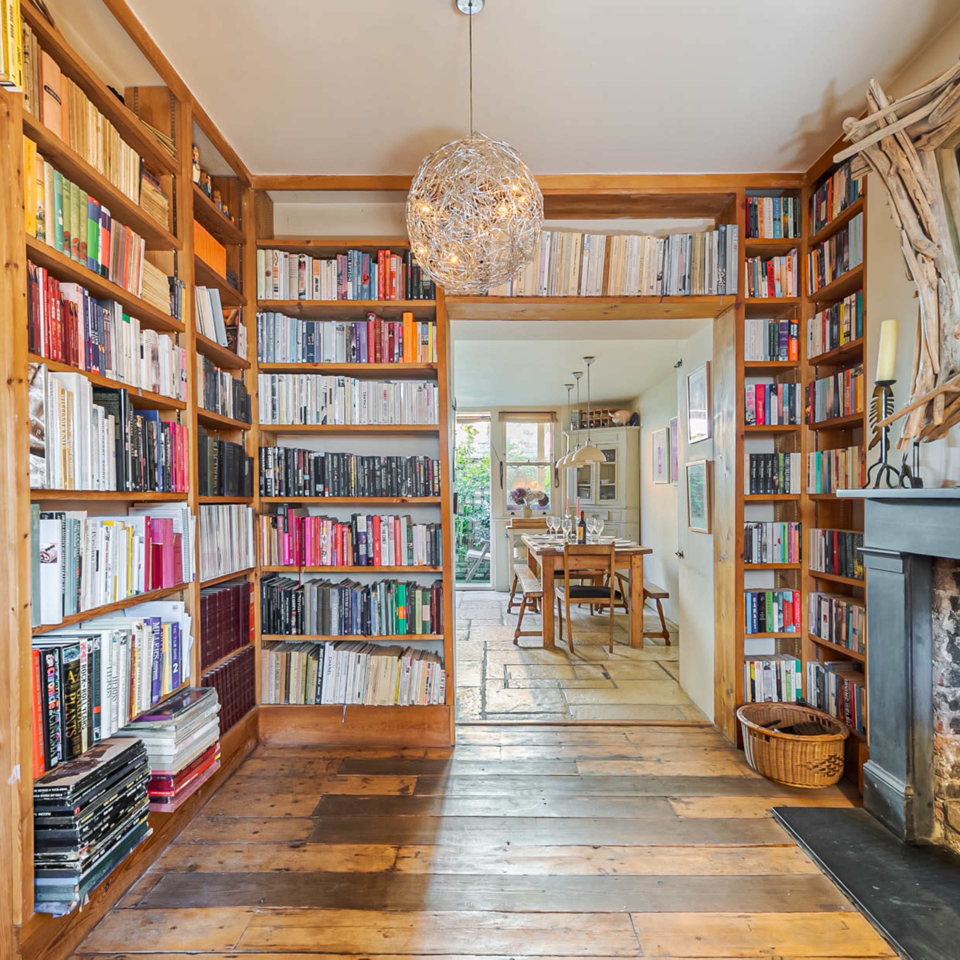 A cozy room features bookshelves filled with colorful books, a wooden floor, and a fireplace.