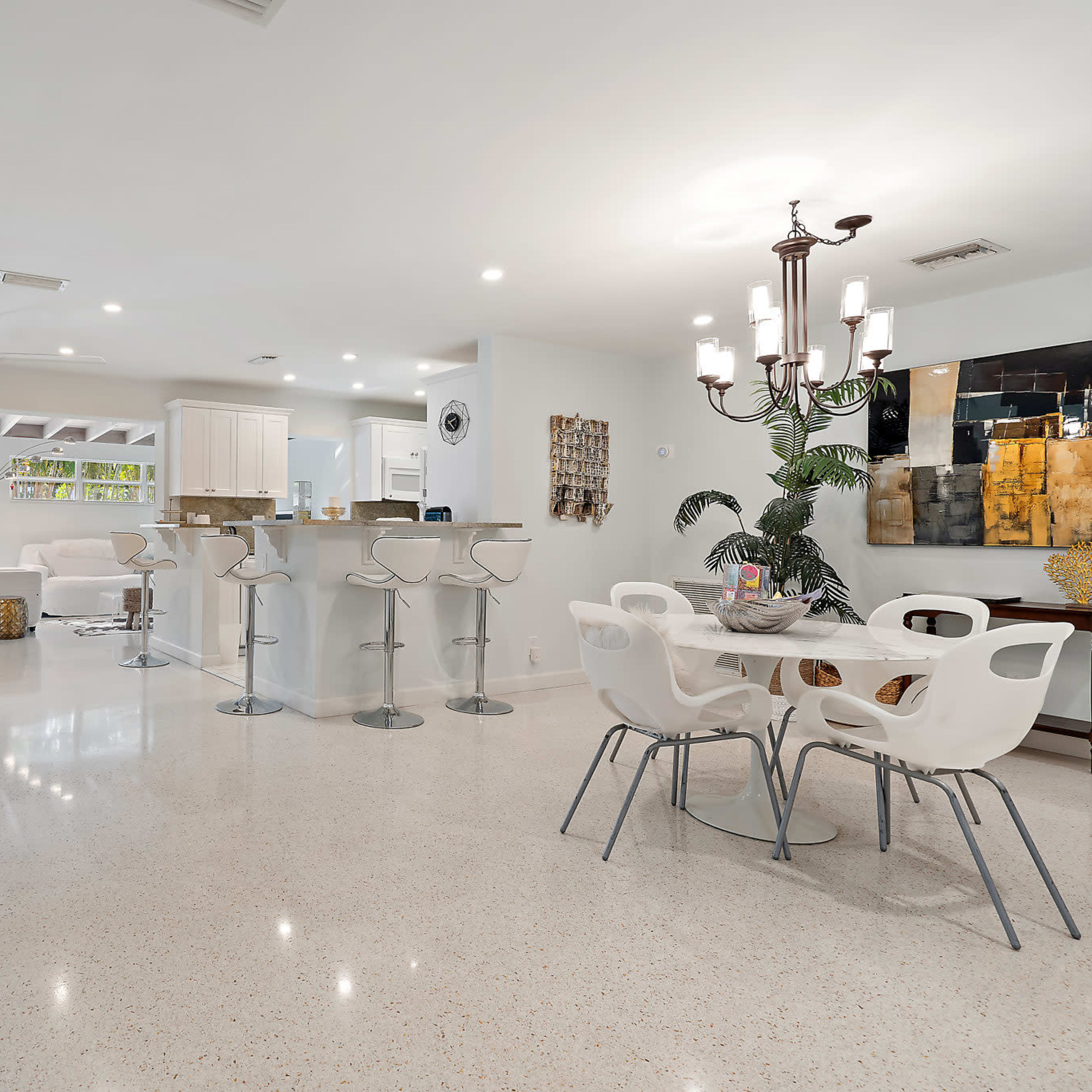 A modern open-concept living area with a white kitchen, bar seating, and a dining table.