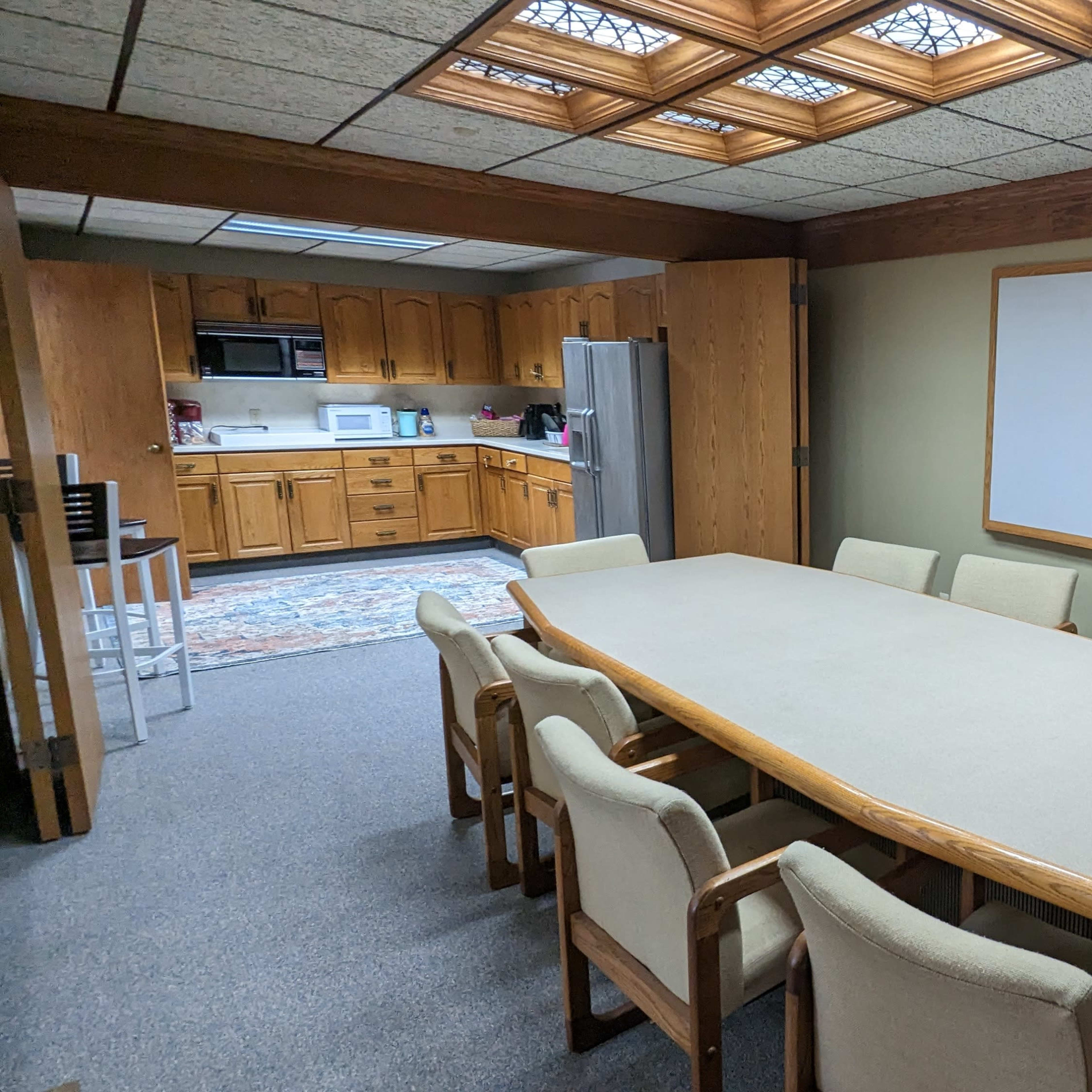 A conference room with a large table surrounded by eight chairs, adjacent to a kitchen area.
