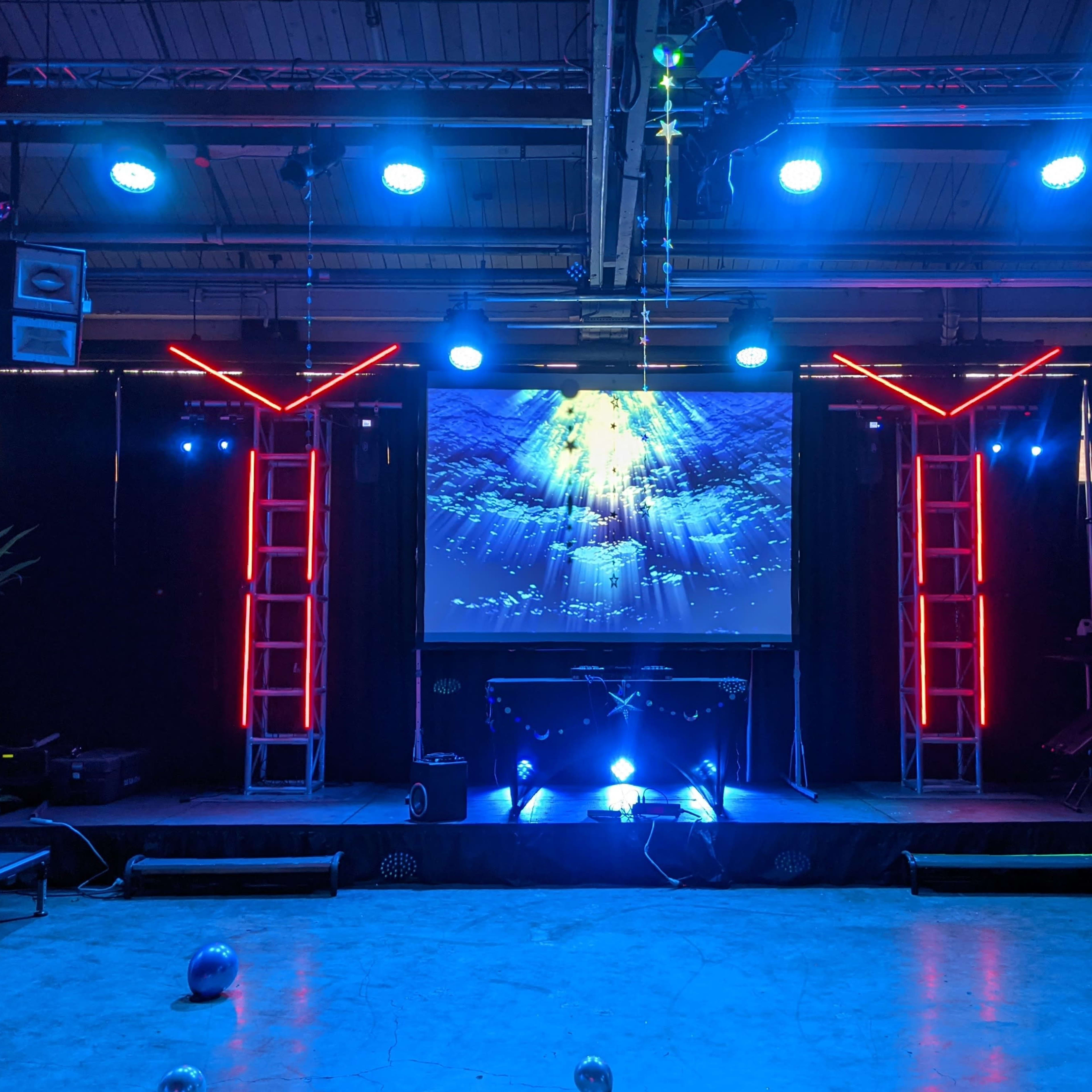 A stage setup with a large screen displaying an underwater scene, surrounded by illuminated frameworks and various lighting fixtures.