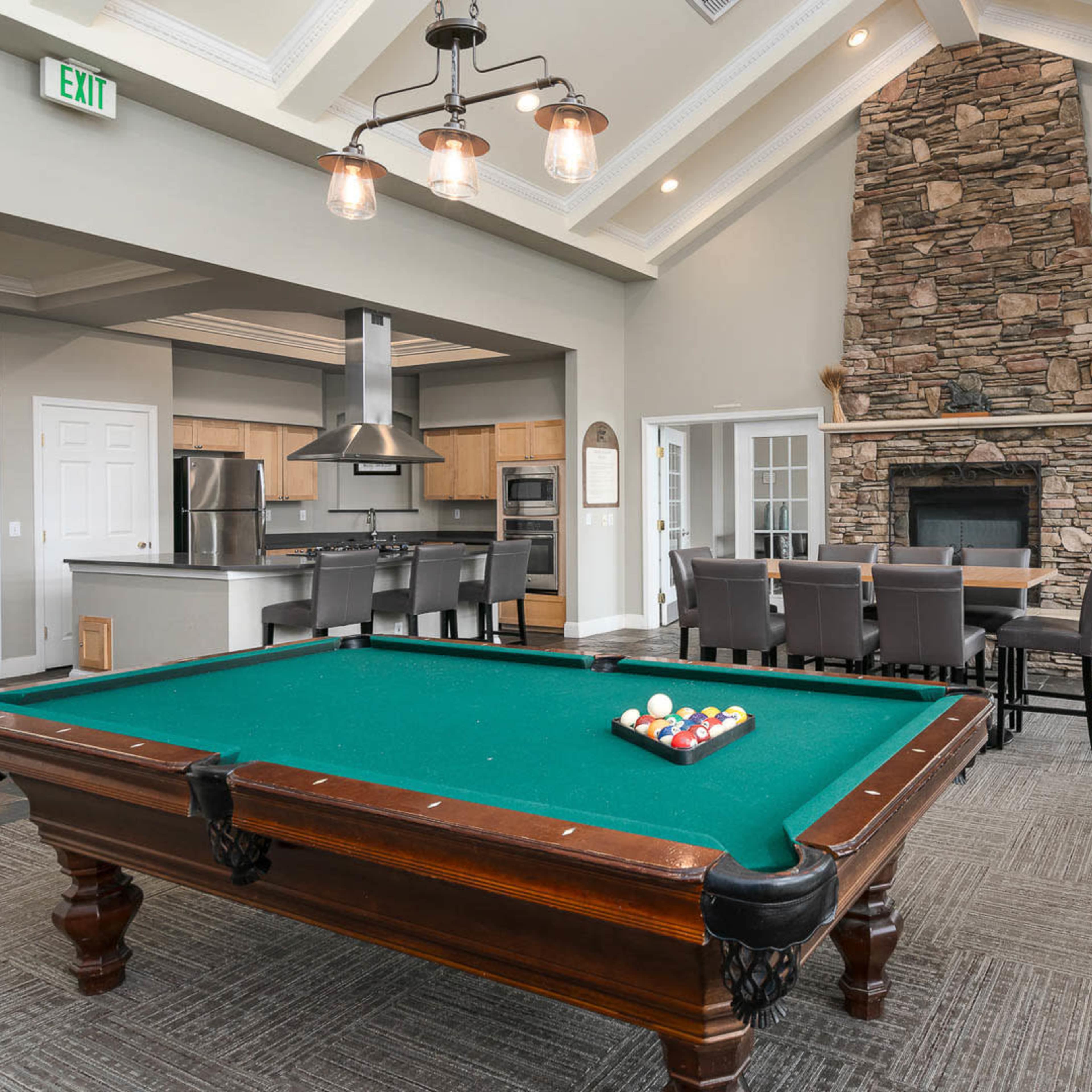 A lounge area featuring a pool table, foosball table, and a stone fireplace, with dining seating in the background.