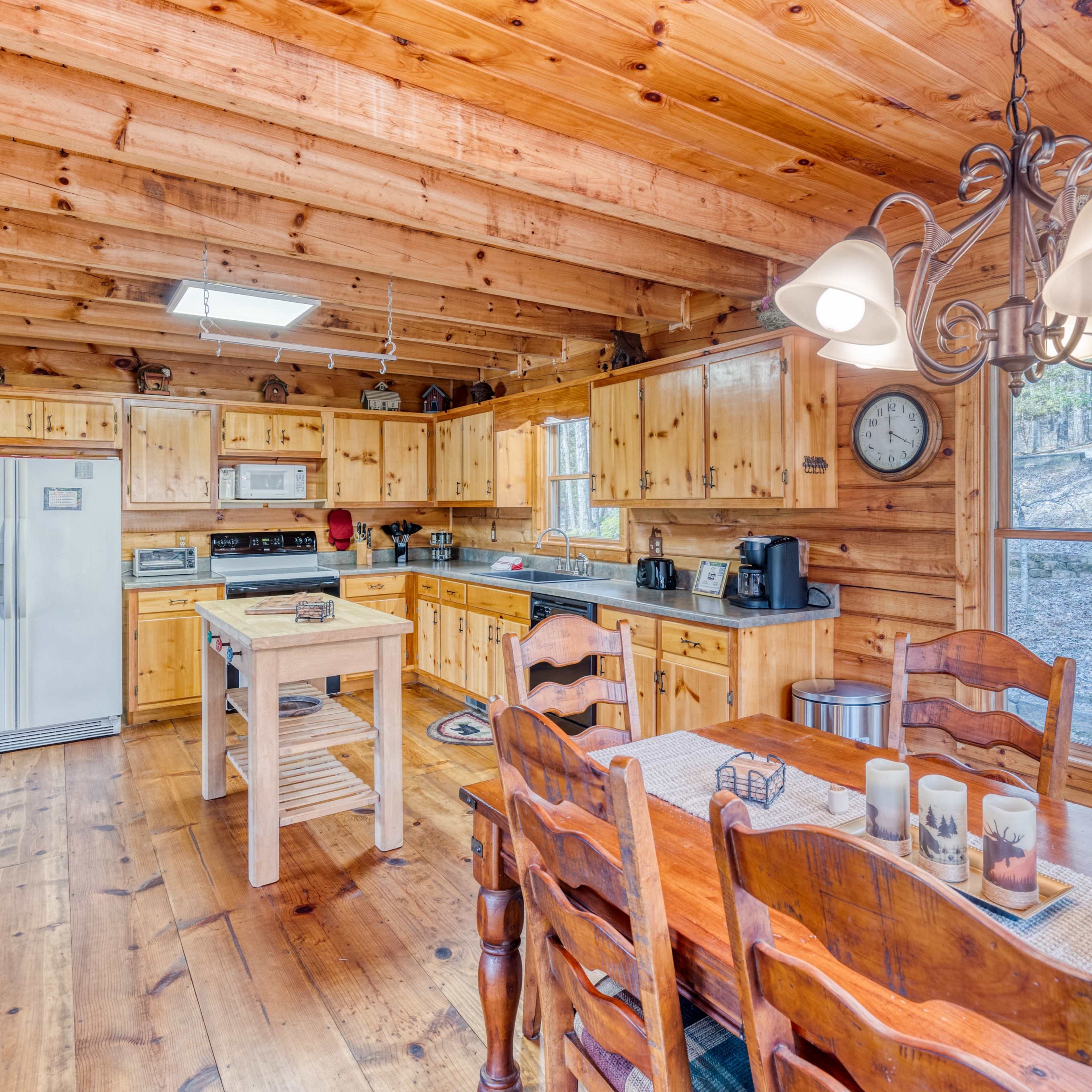 A wooden kitchen and dining area featuring a central table with chairs, a kitchen island, and exposed wooden beams on the ceiling.
