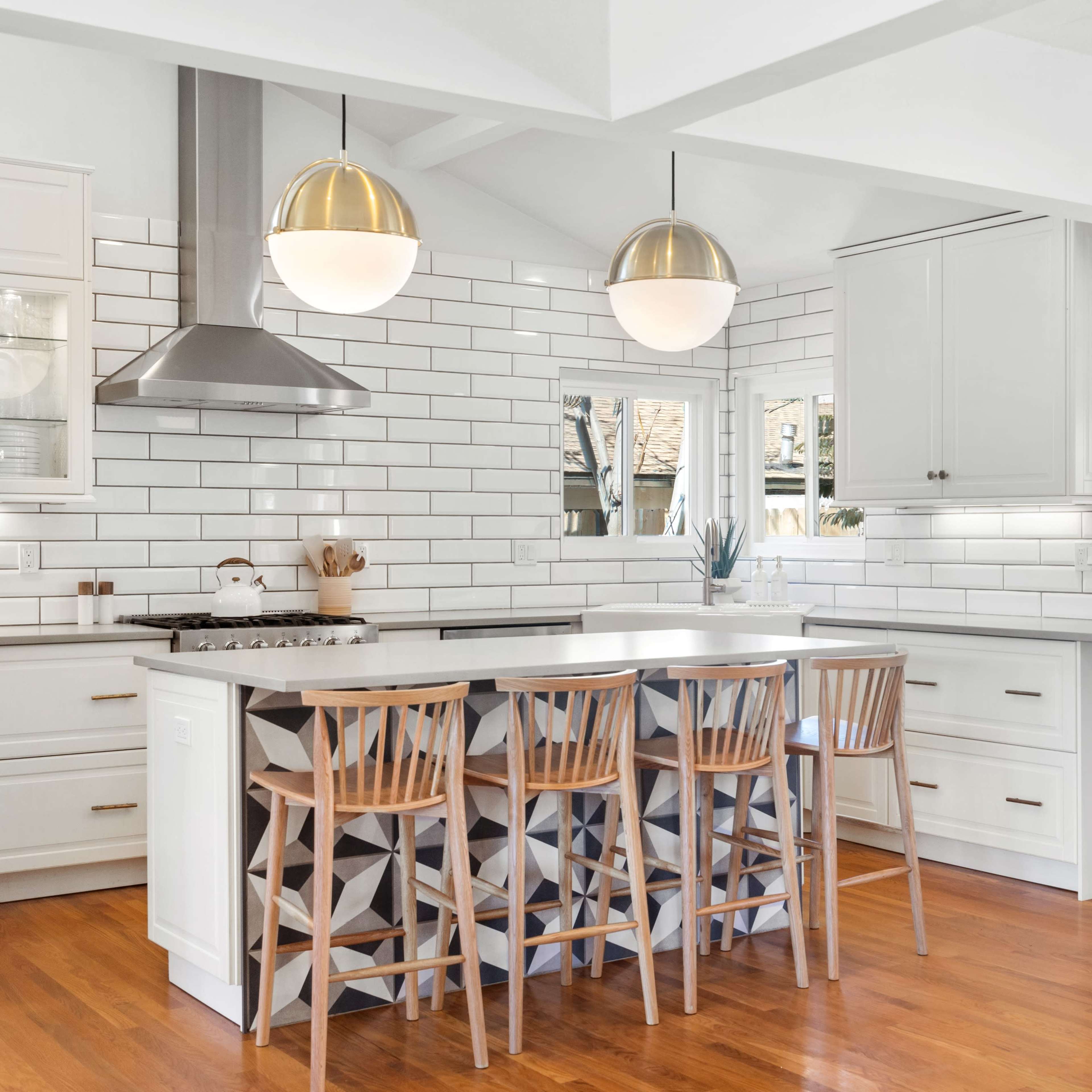 A modern kitchen featuring white cabinetry, a central island with wooden stools, and backsplash tiles arranged in a grid pattern.