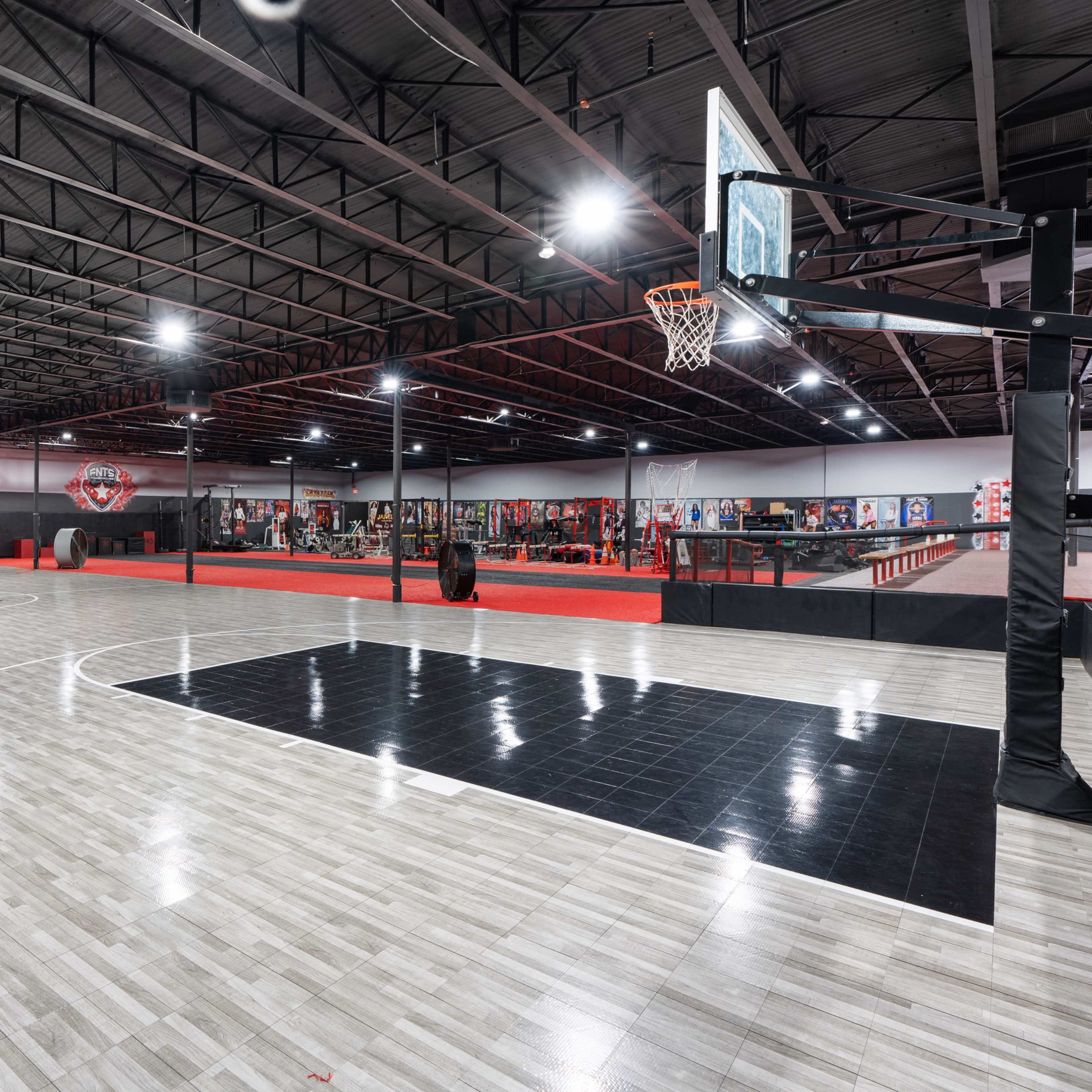 A spacious indoor basketball court with marked lines, basketball hoops at either end, and orange cones placed around the perimeter.