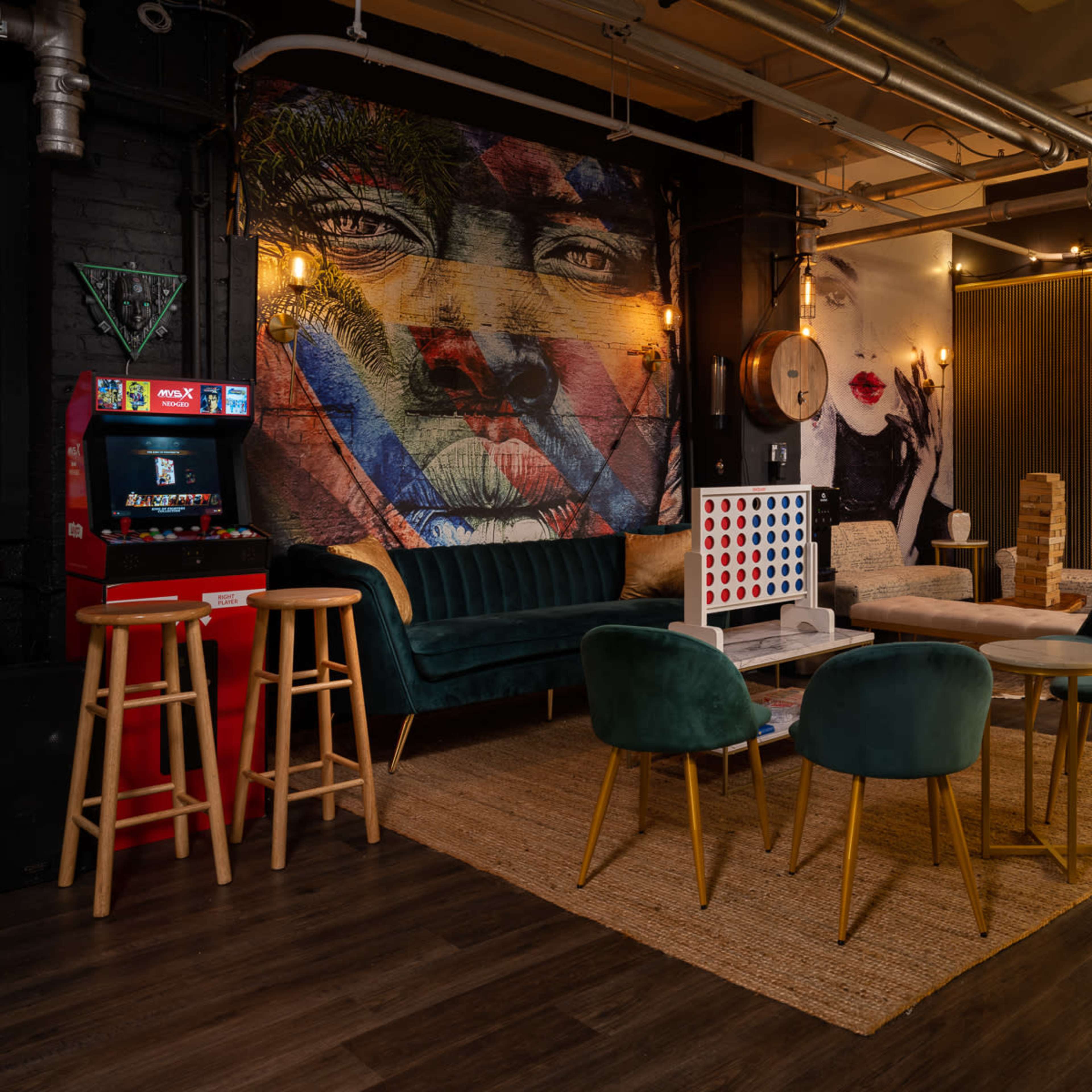 A stylish lounge area featuring a mix of seating options, vibrant murals on the walls, and a vintage arcade game.
