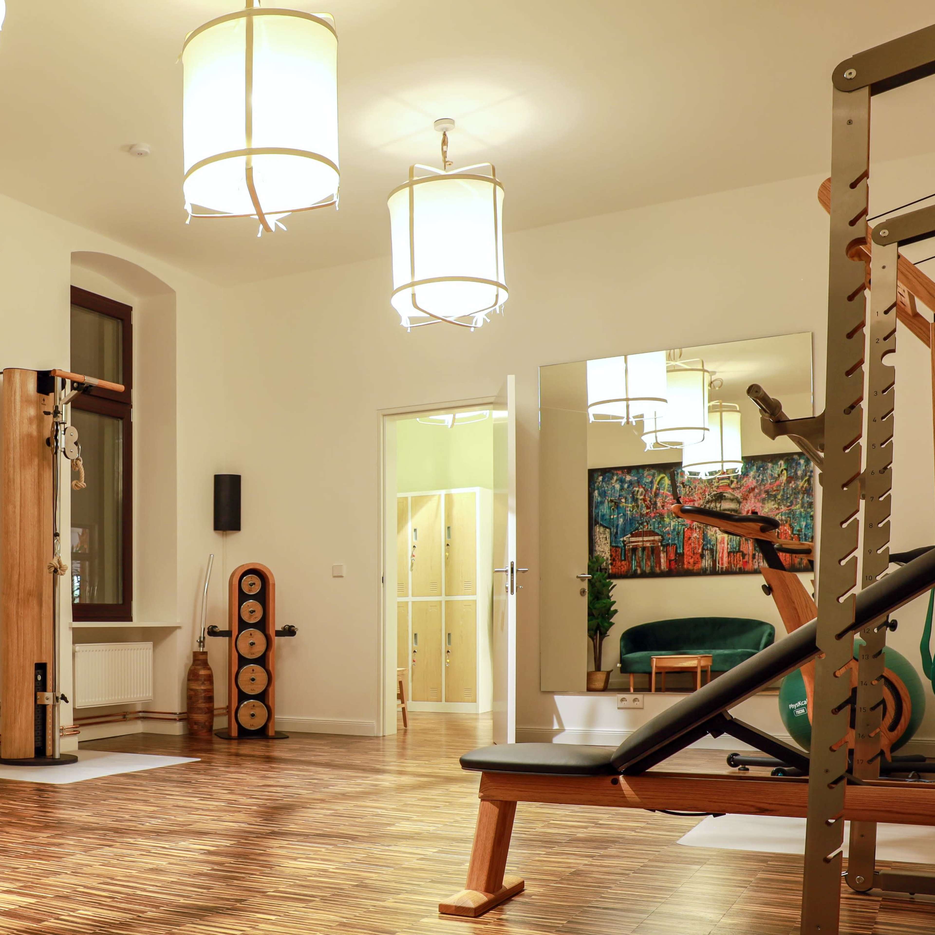 A spacious indoor fitness studio with wooden floors, multiple light fixtures, exercise equipment, and a large mirror.