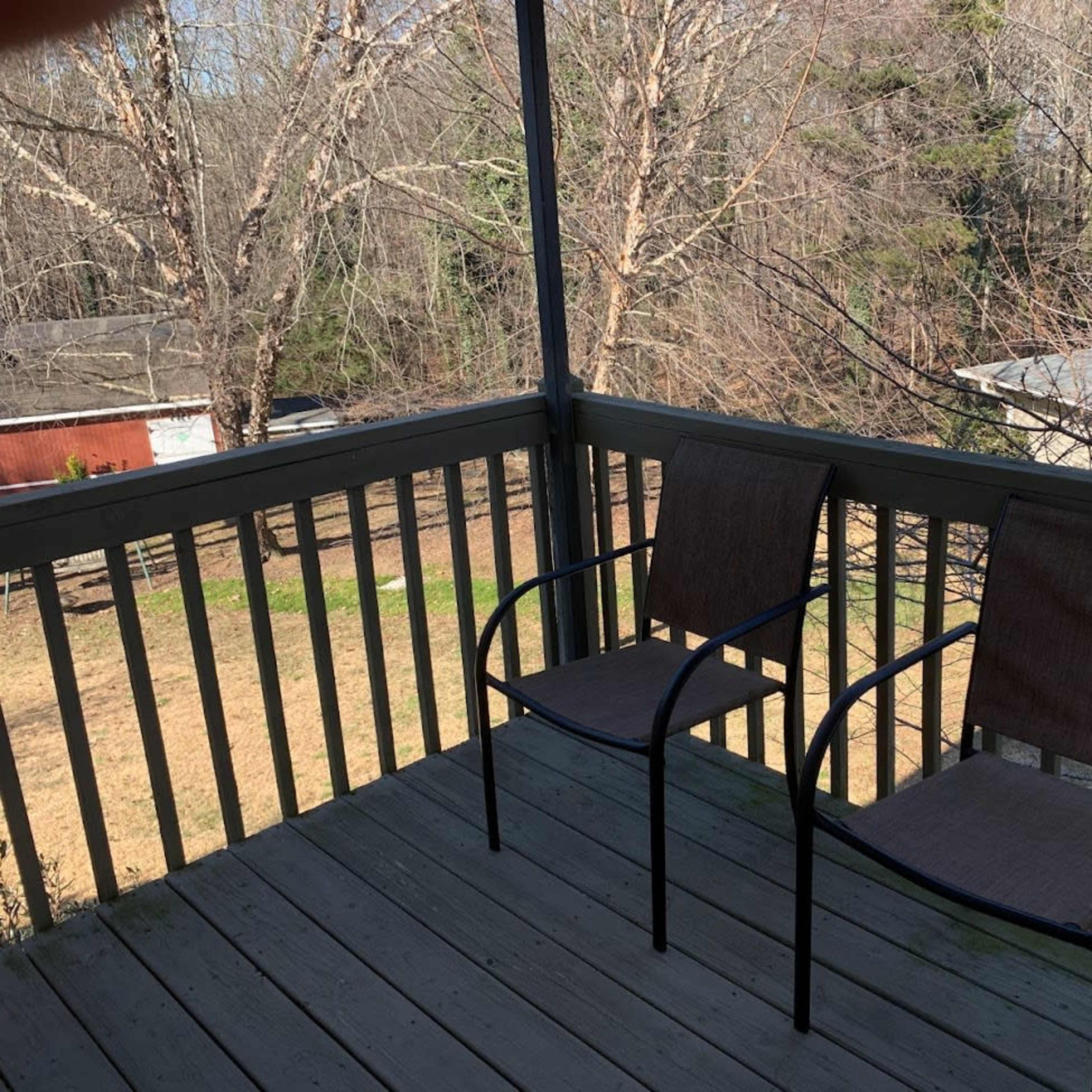 A porch with two empty chairs overlooking a grassy area and trees in the background.