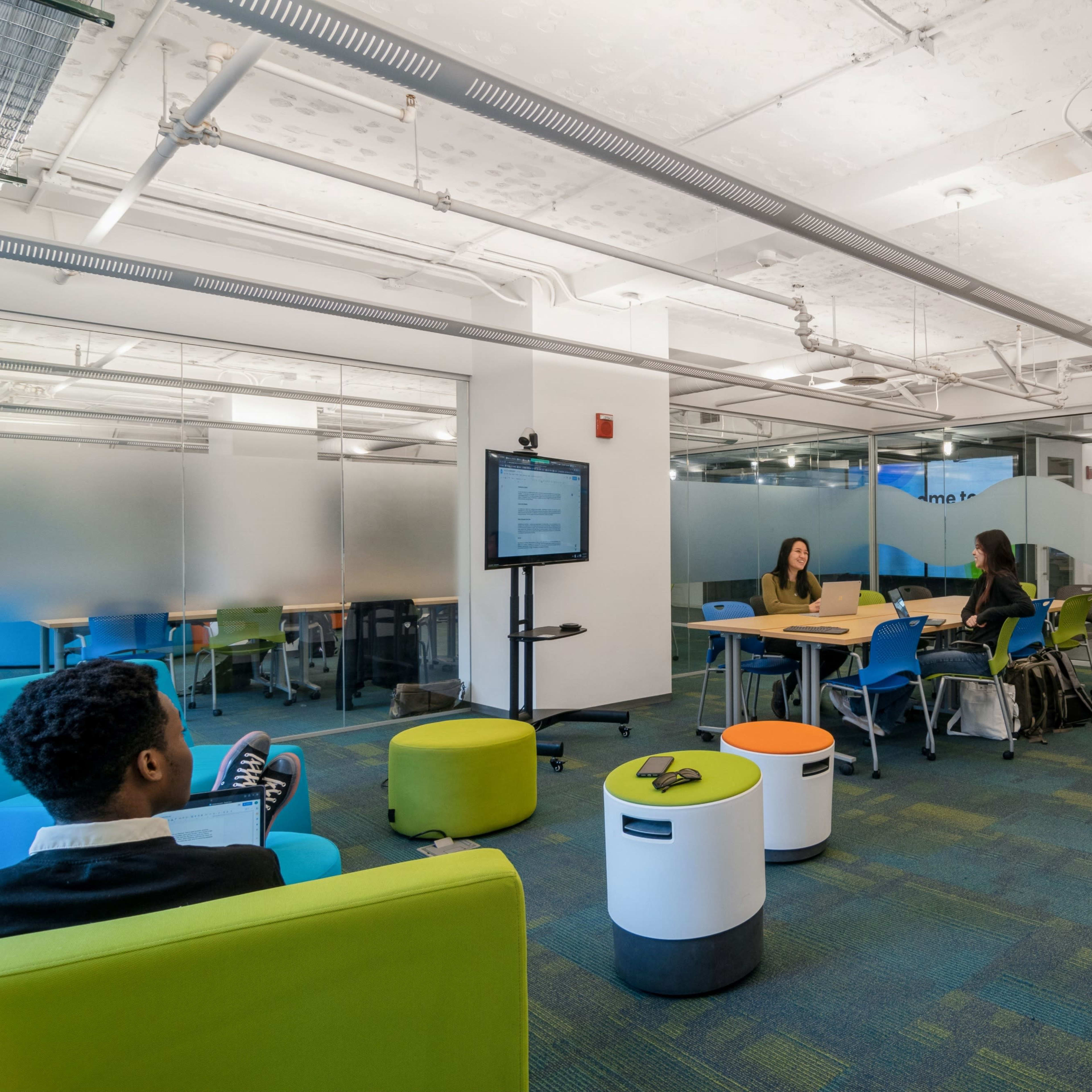 A group of students collaborates in a modern study area with colorful seating and a whiteboard.