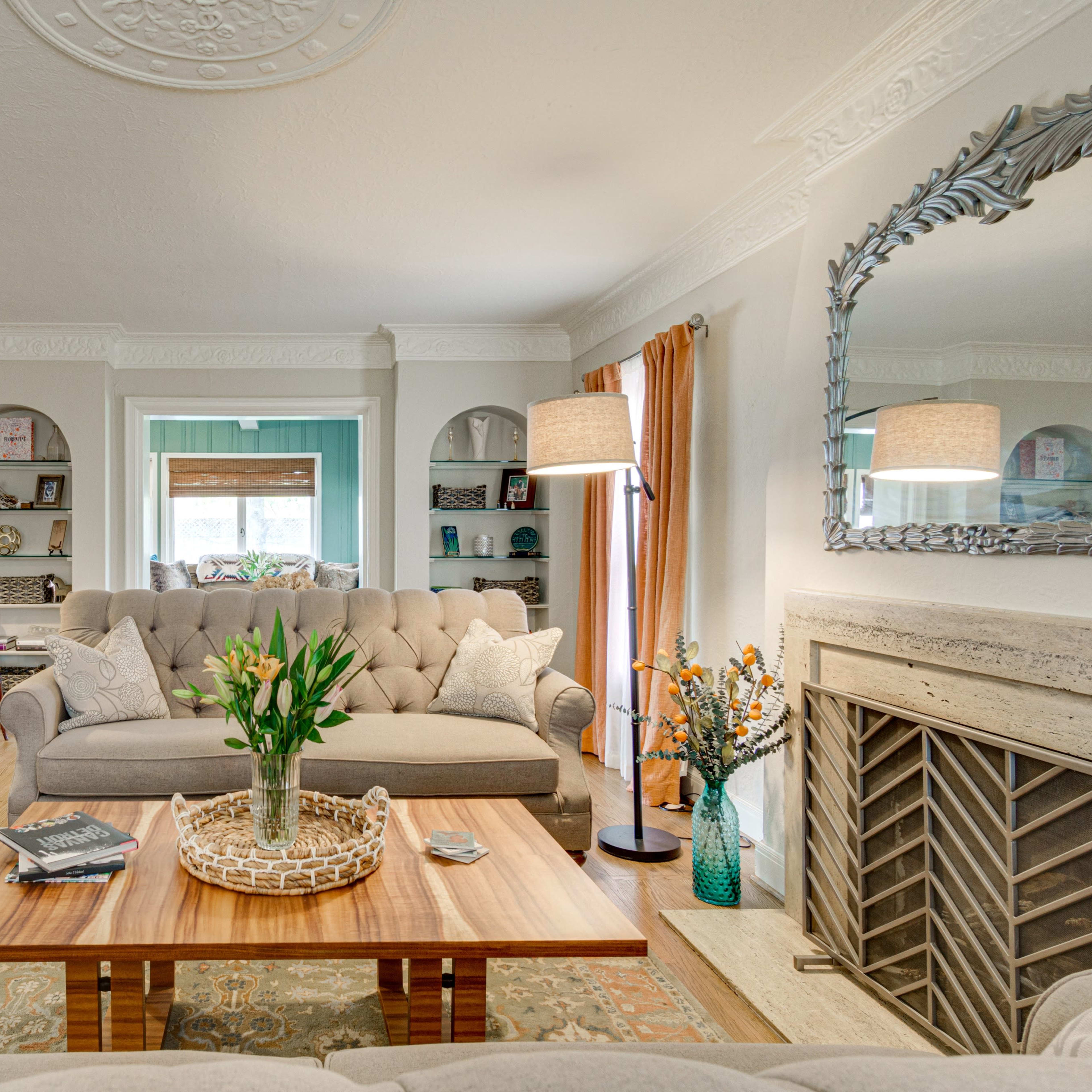 A well-furnished living room features a beige couch, a wooden coffee table with a decorative tray, and a fireplace surrounded by built-in shelves and art.