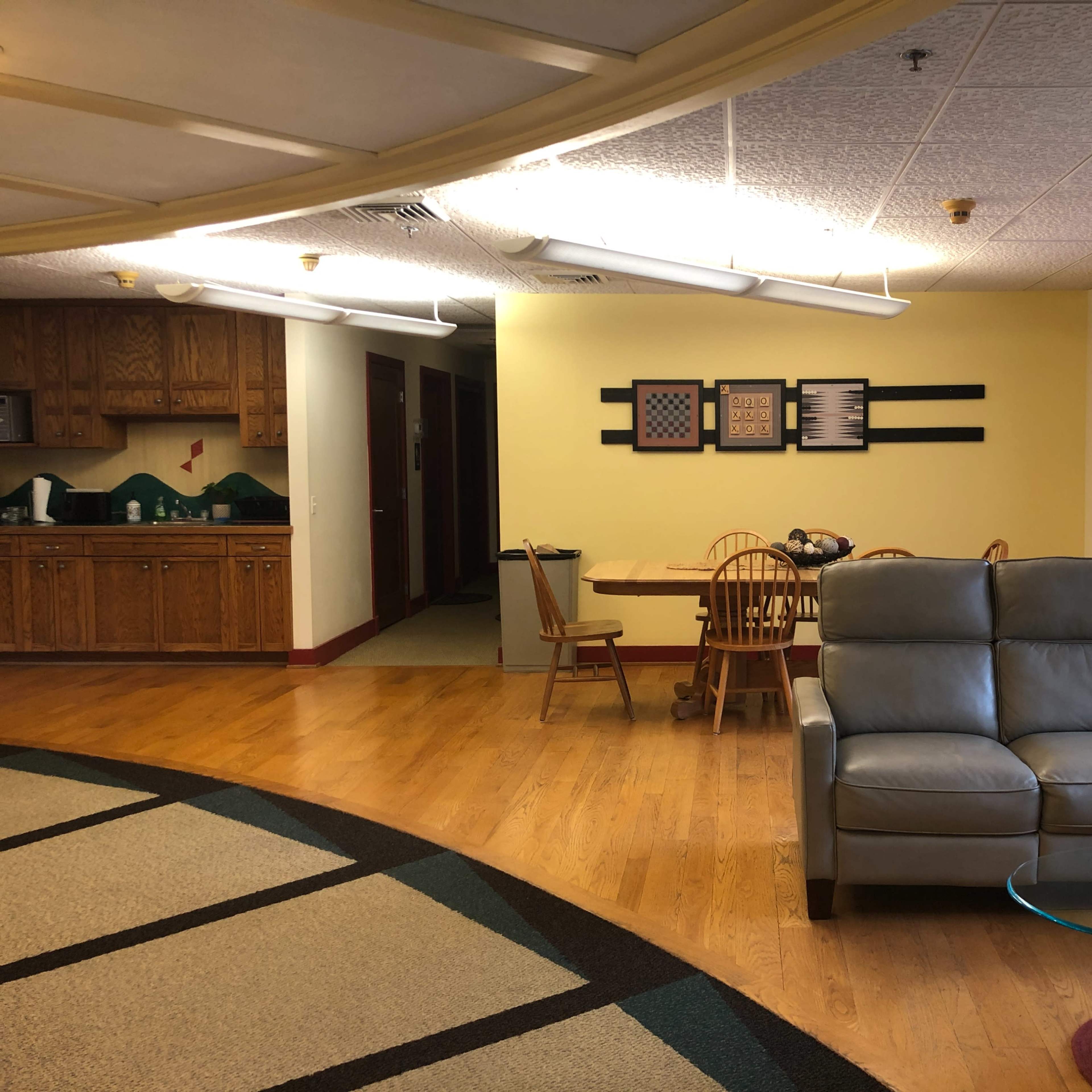 A communal living area with a light-colored kitchen, dining table, and a gray sofa.