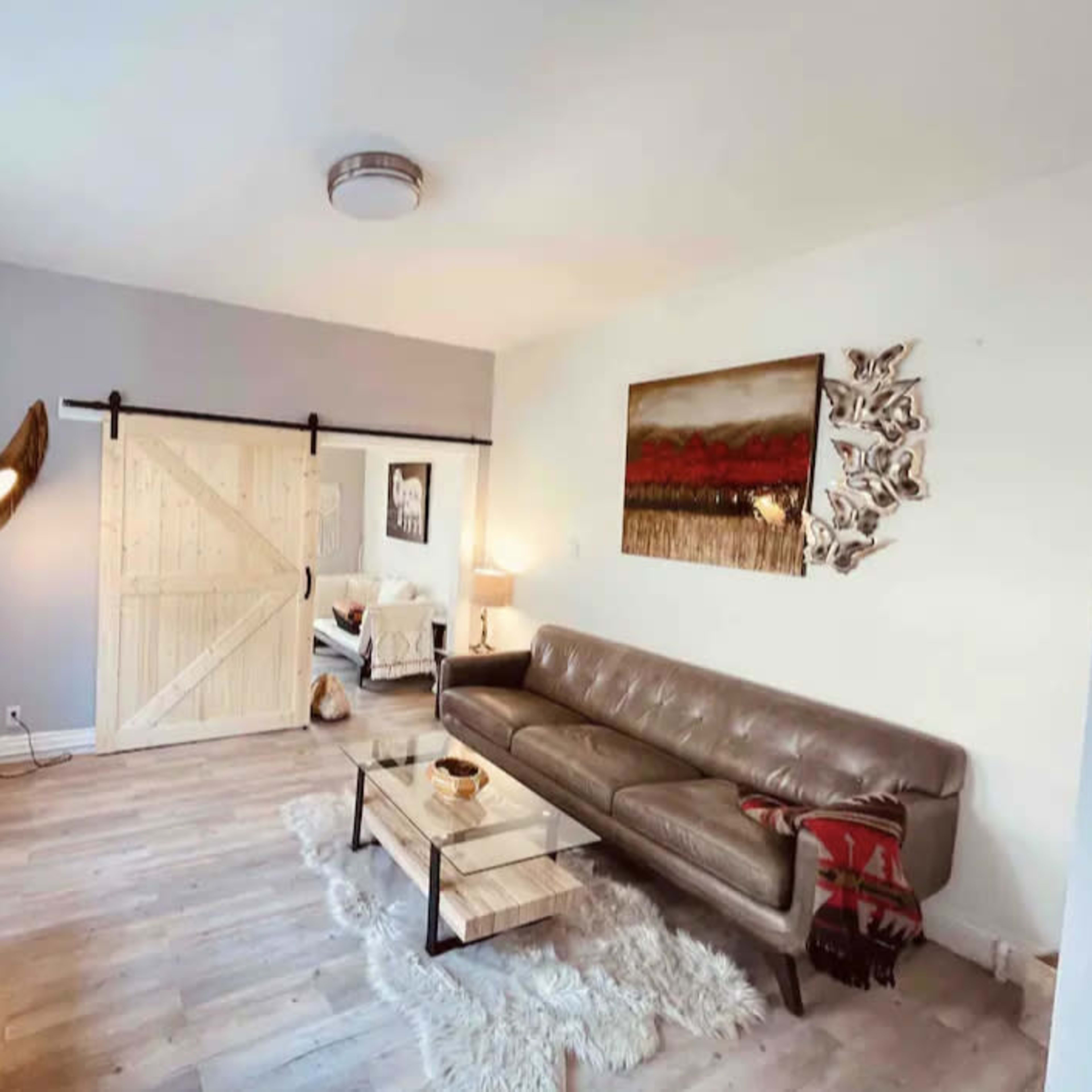 A modern living room featuring a leather sofa, a wooden barn door, a glass coffee table, and decorative wall art.