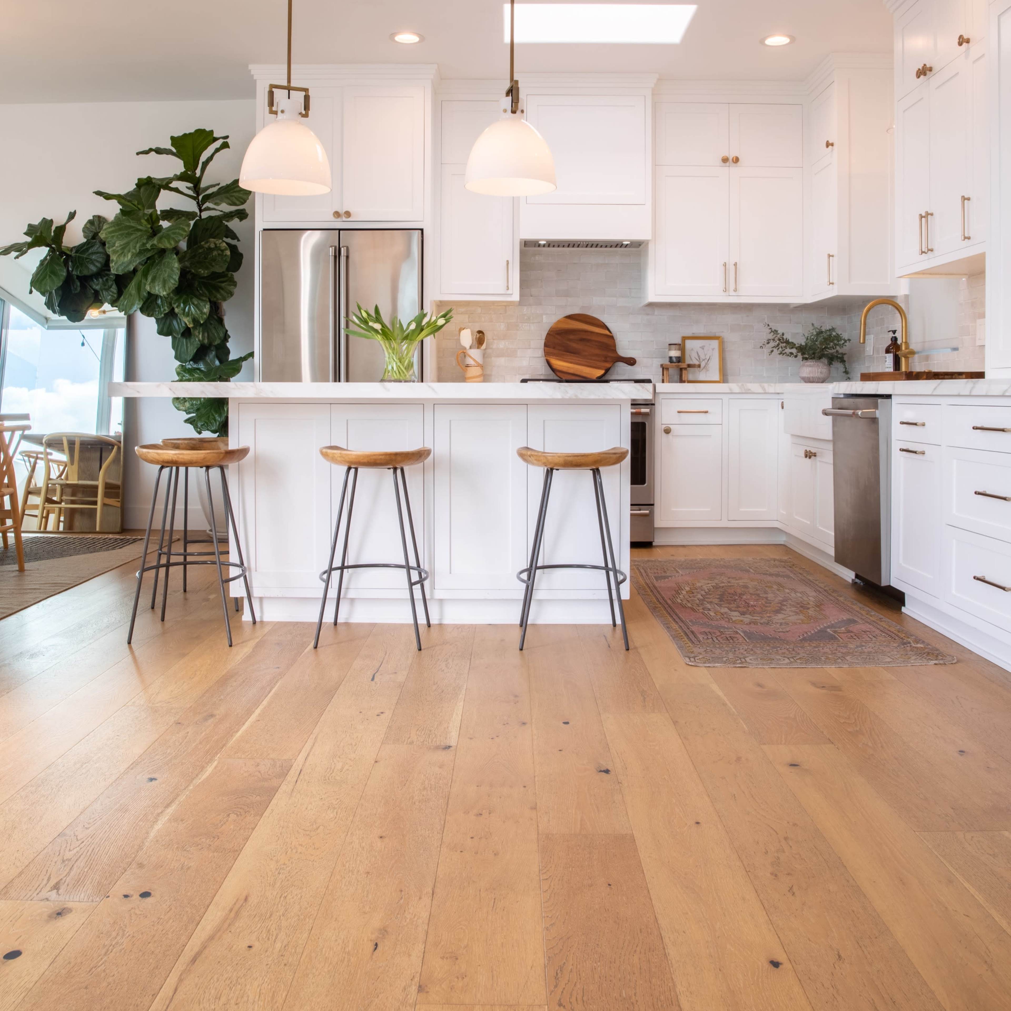 A modern kitchen featuring white cabinetry, a central island with three bar stools, and large windows that allow natural light to enter.