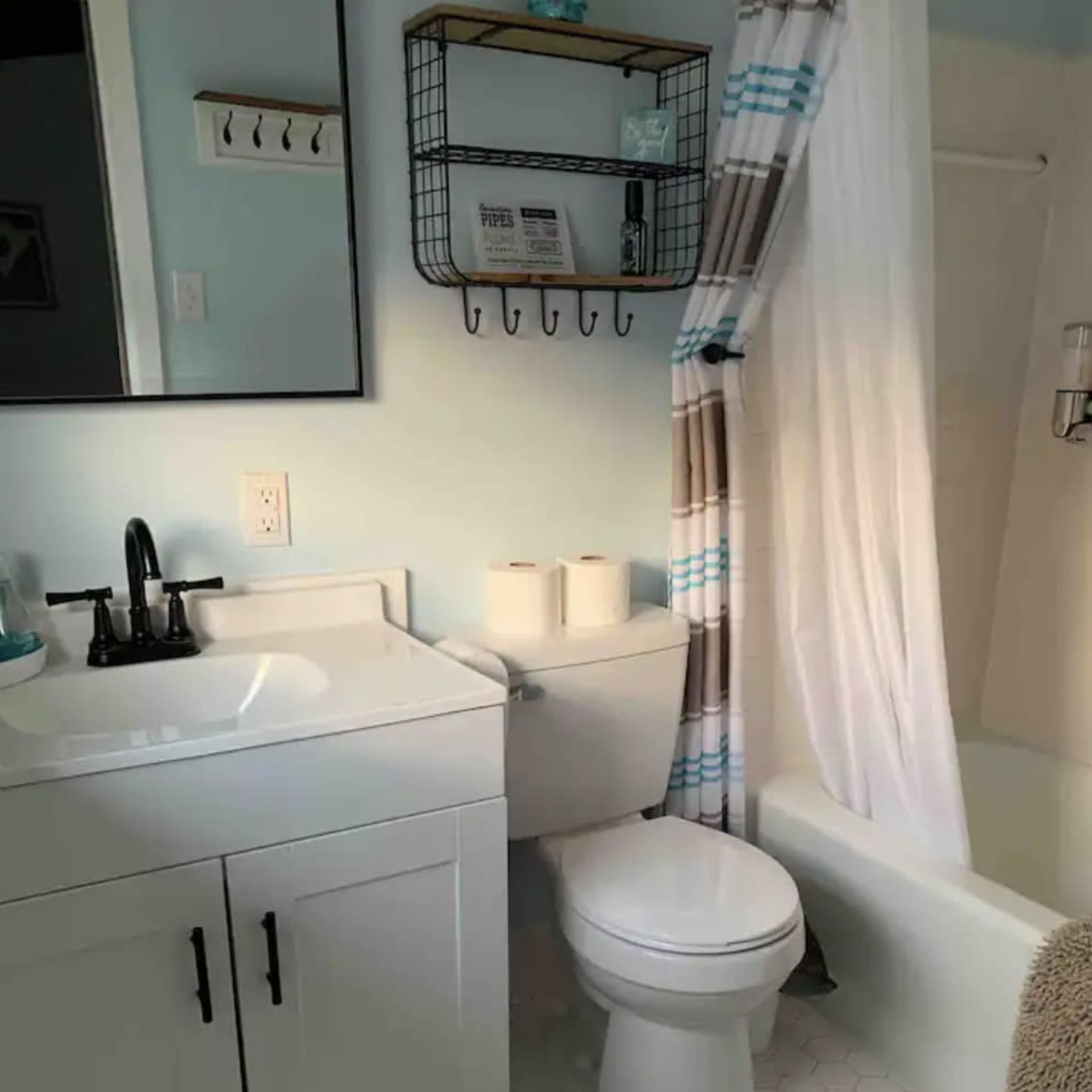 The bathroom features a white vanity with a black faucet, a toilet, and a bathtub with a shower curtain, all arranged around hexagonal tiled flooring.