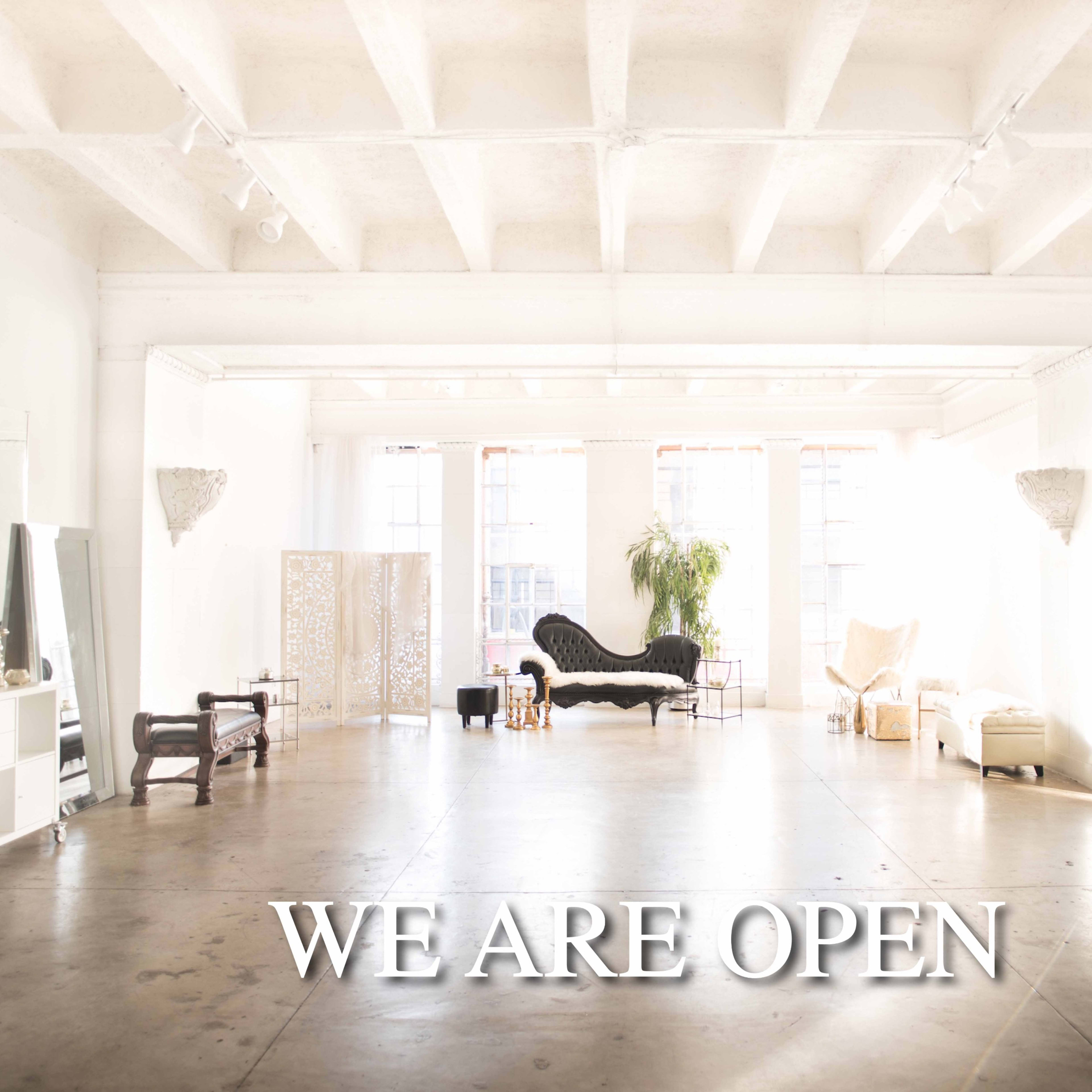 A spacious, bright interior features various seating arrangements and mirrors, with the phrase "WE ARE OPEN" prominently displayed.