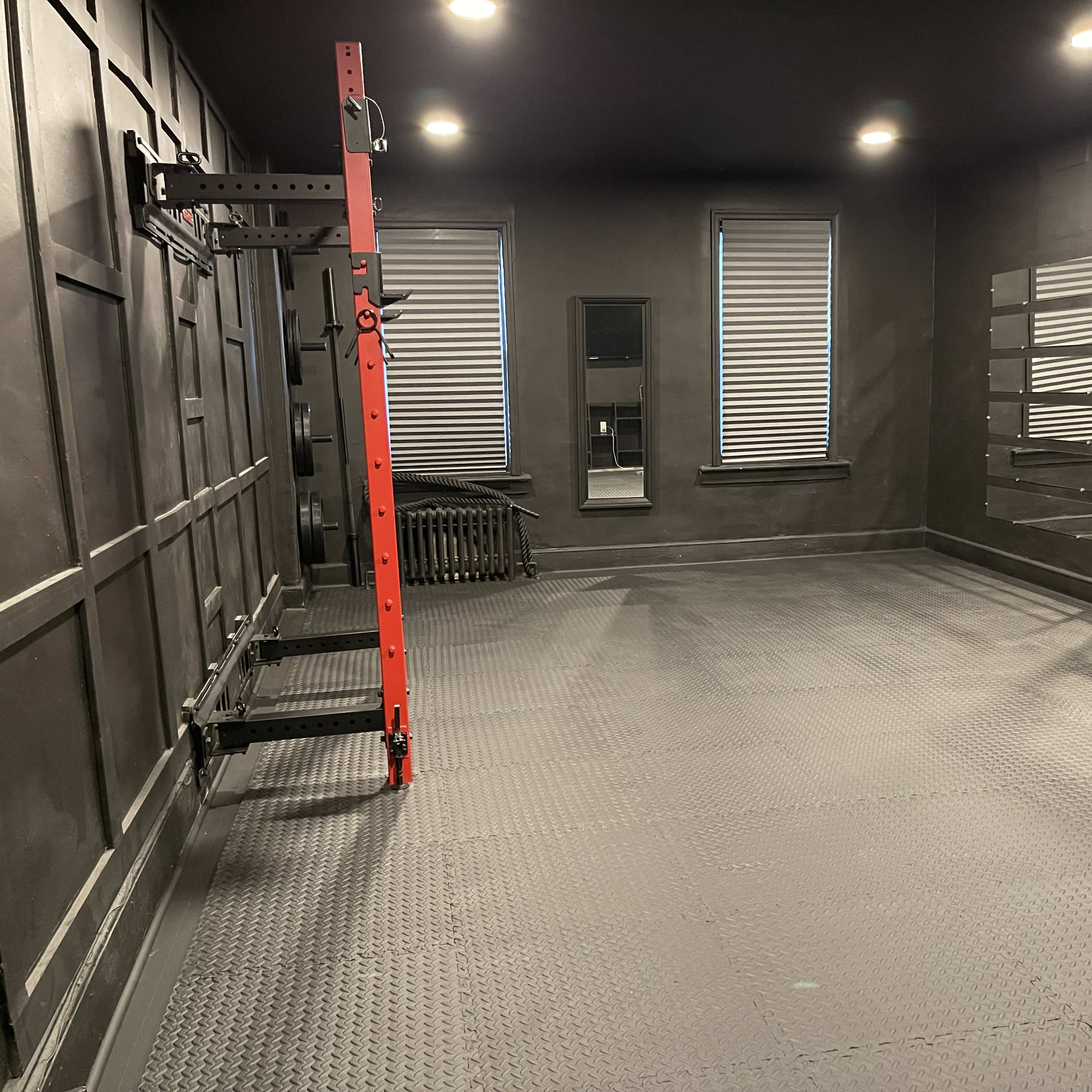 An empty room with black walls and flooring, featuring a red rack on one side and mirrors on the opposite wall.