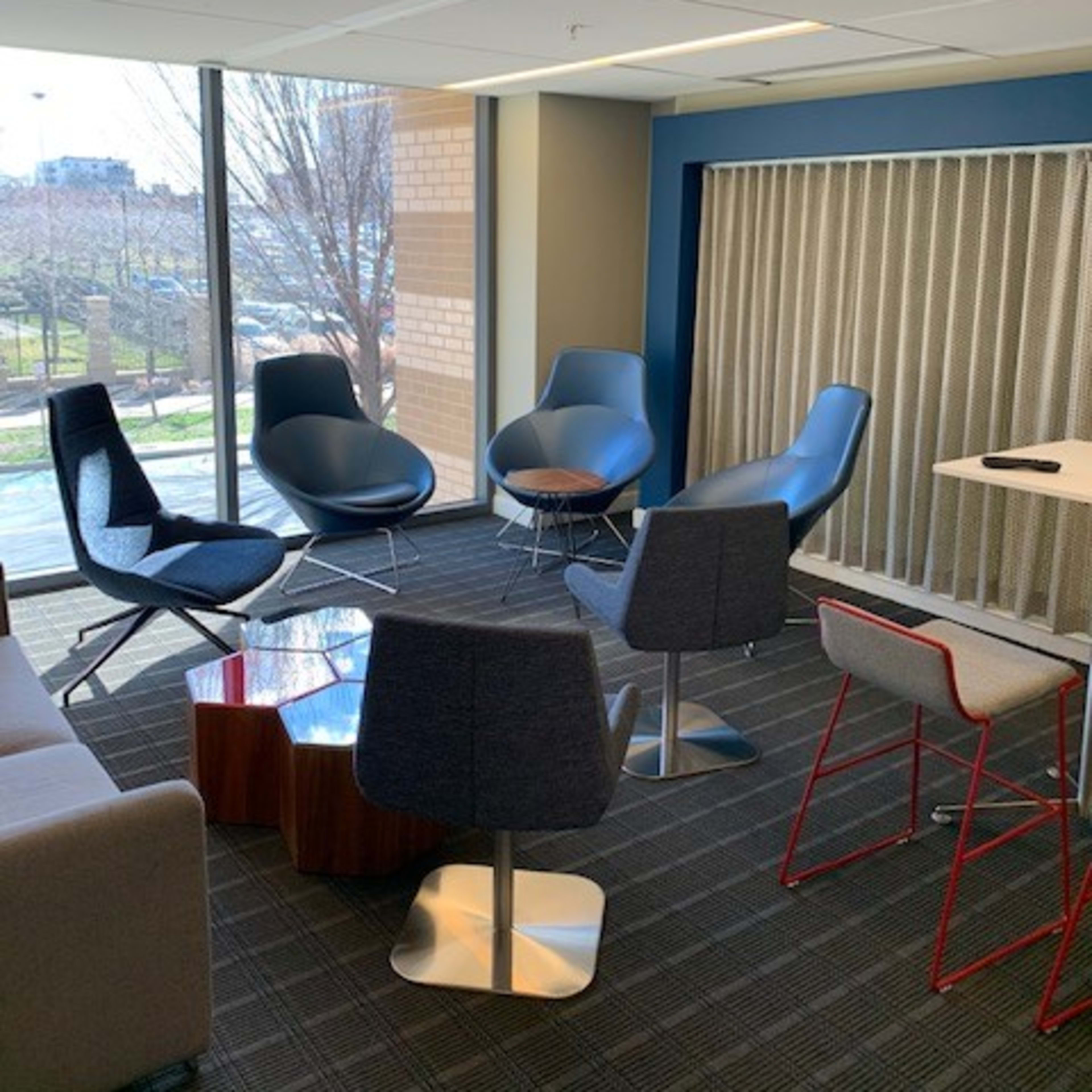 A modern office space with several stylish chairs arranged around a small table near large windows.