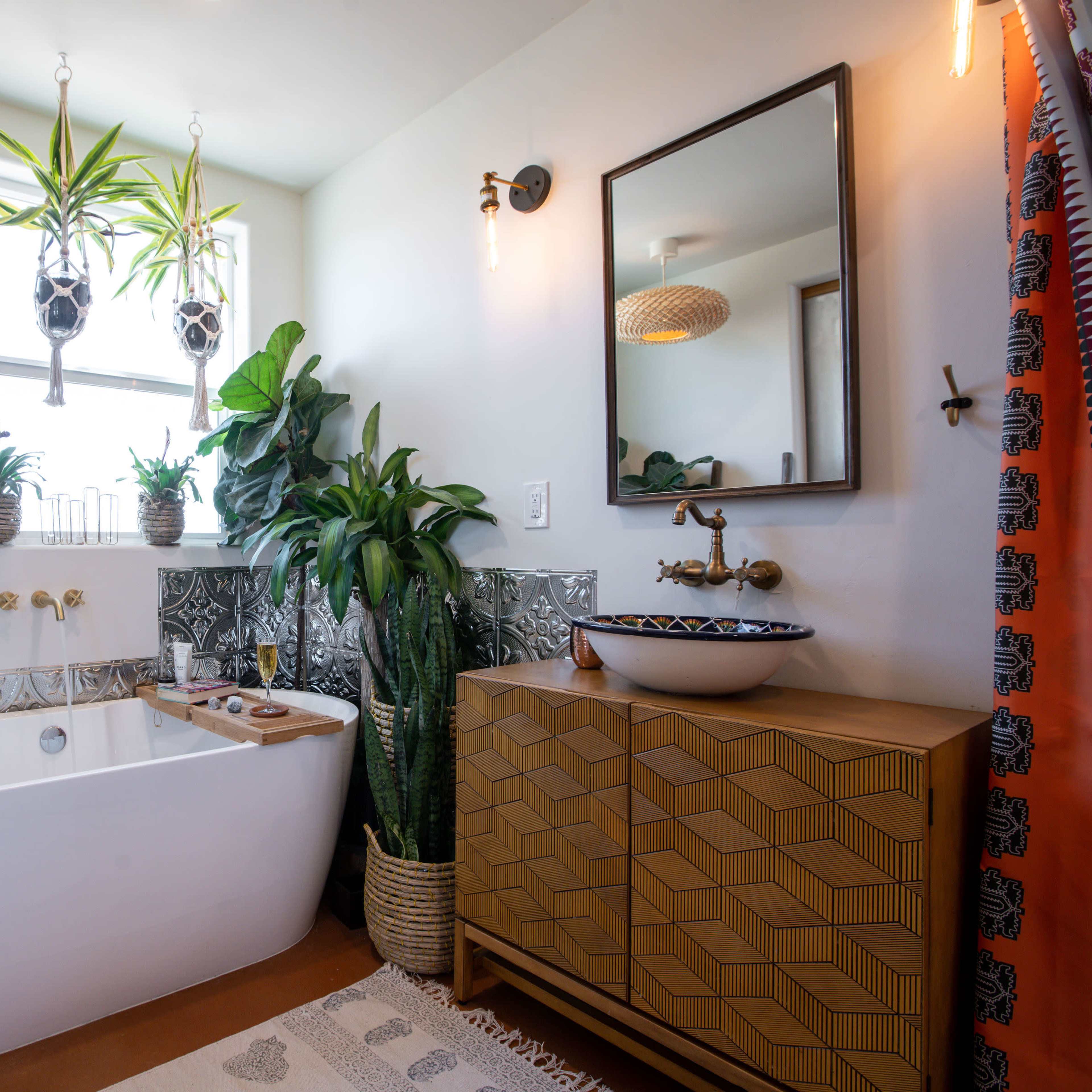 A modern bathroom featuring a freestanding bathtub, a wooden vanity with a vessel sink, indoor plants, and a large window allowing natural light.