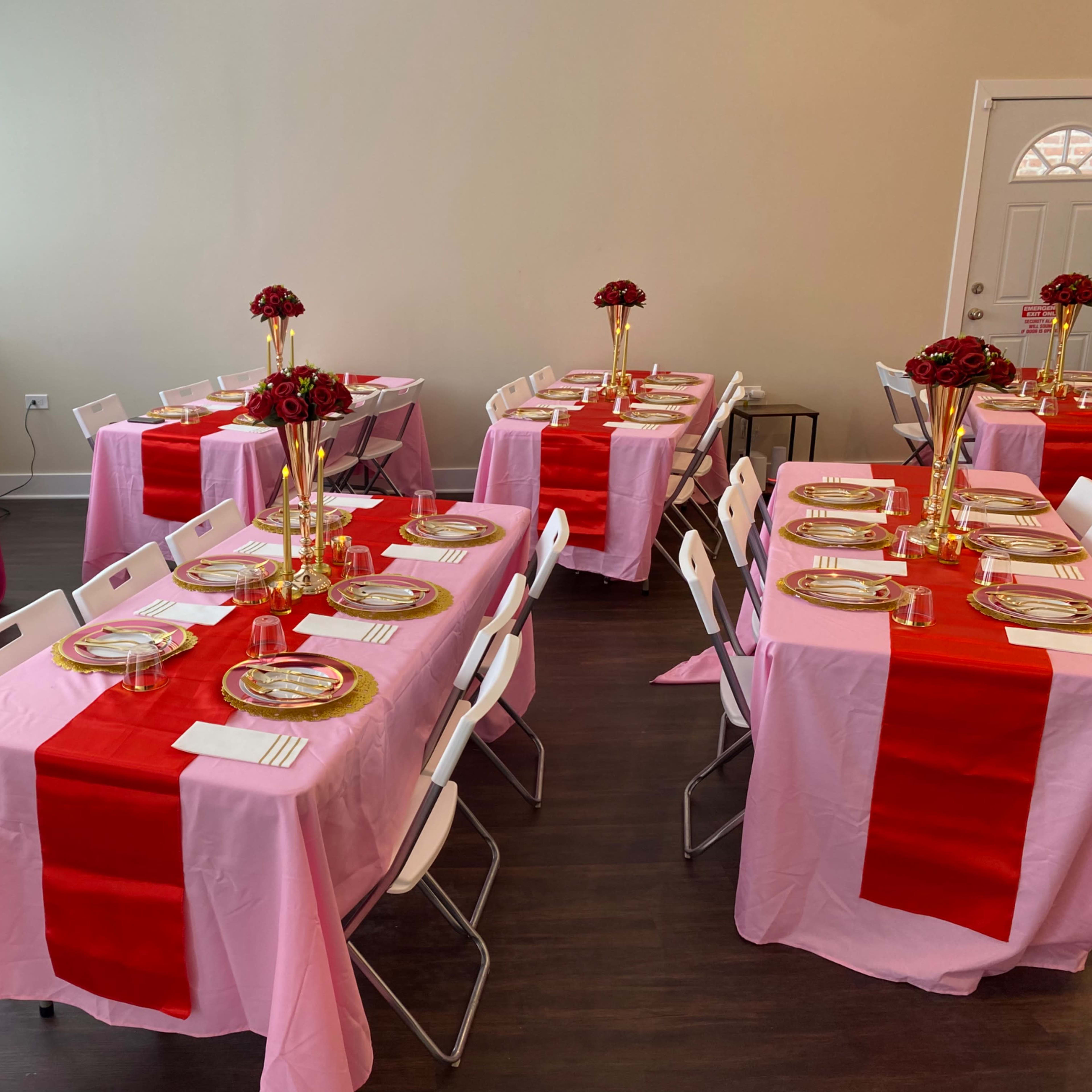 The room features several tables set with pink and red tablecloths, gold dinnerware, and floral centerpieces arranged in vases.