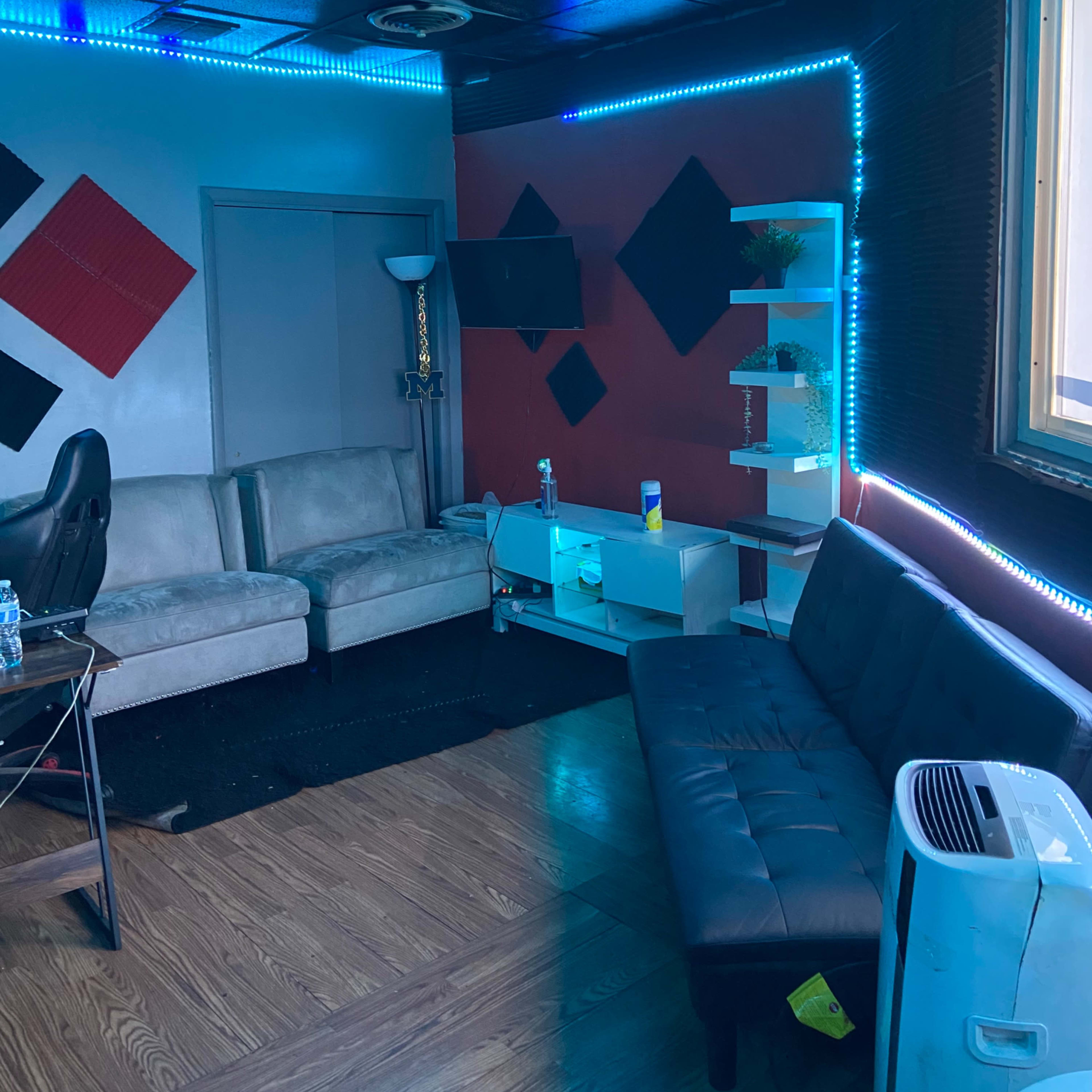 A small room with two sofas, a wall-mounted TV, a shelf with plants, and blue LED lighting.