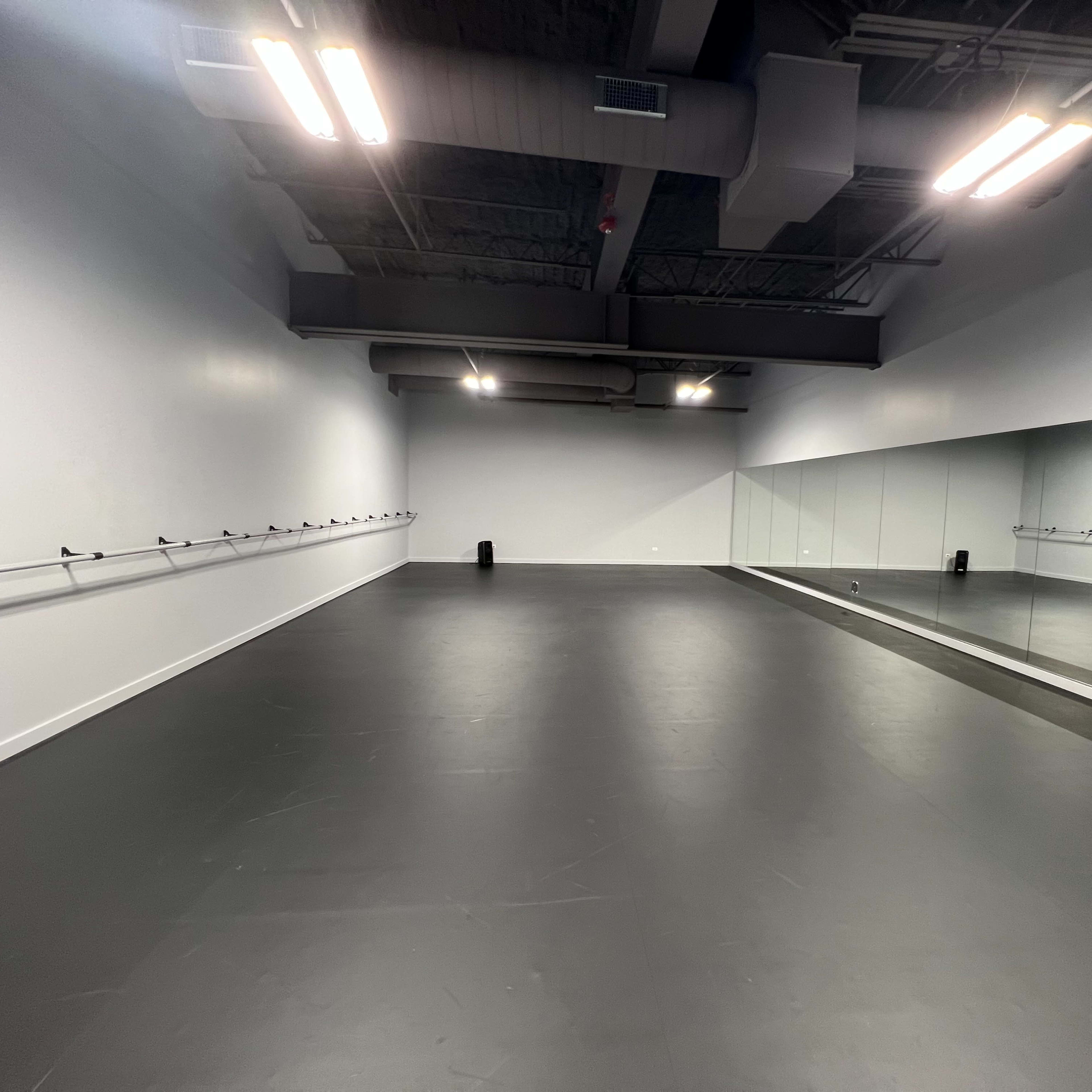 An empty dance studio with a mirrored wall and barre along one side.