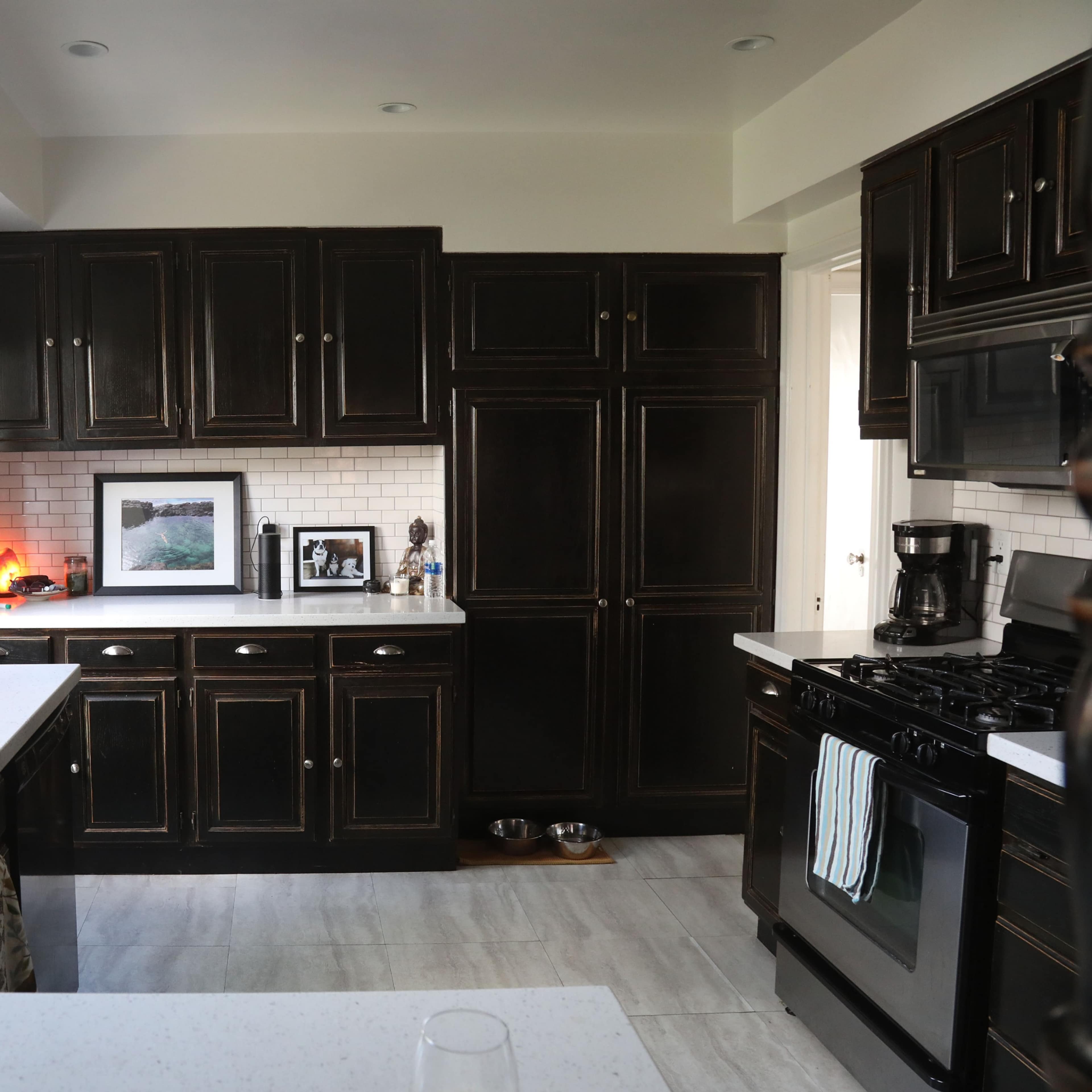 A modern kitchen with dark cabinetry, white countertops, and a tiled backsplash, featuring a sink and stove on opposite sides.