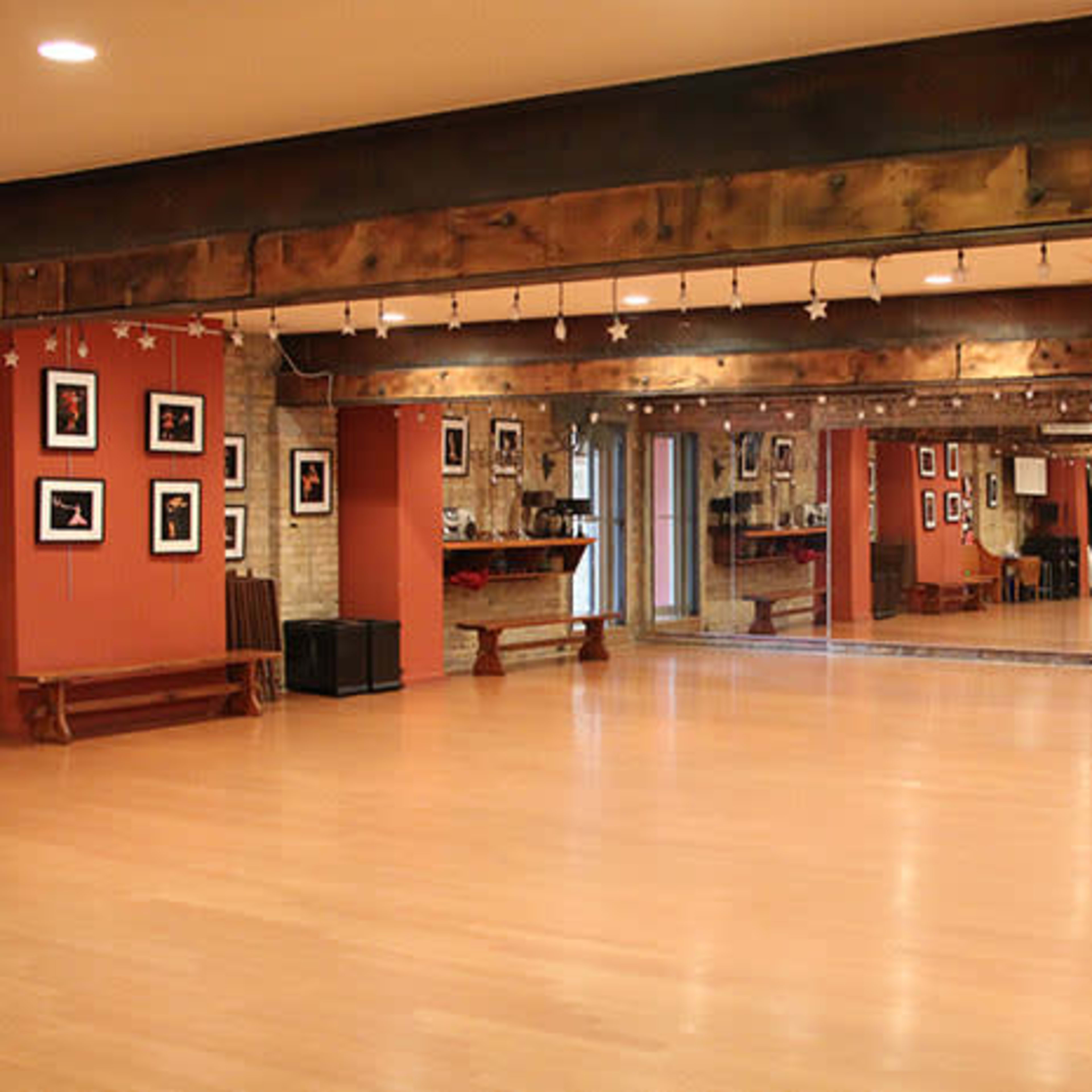 A spacious dance studio with wooden beams, mirrored walls, and framed photographs lining the reddish walls.