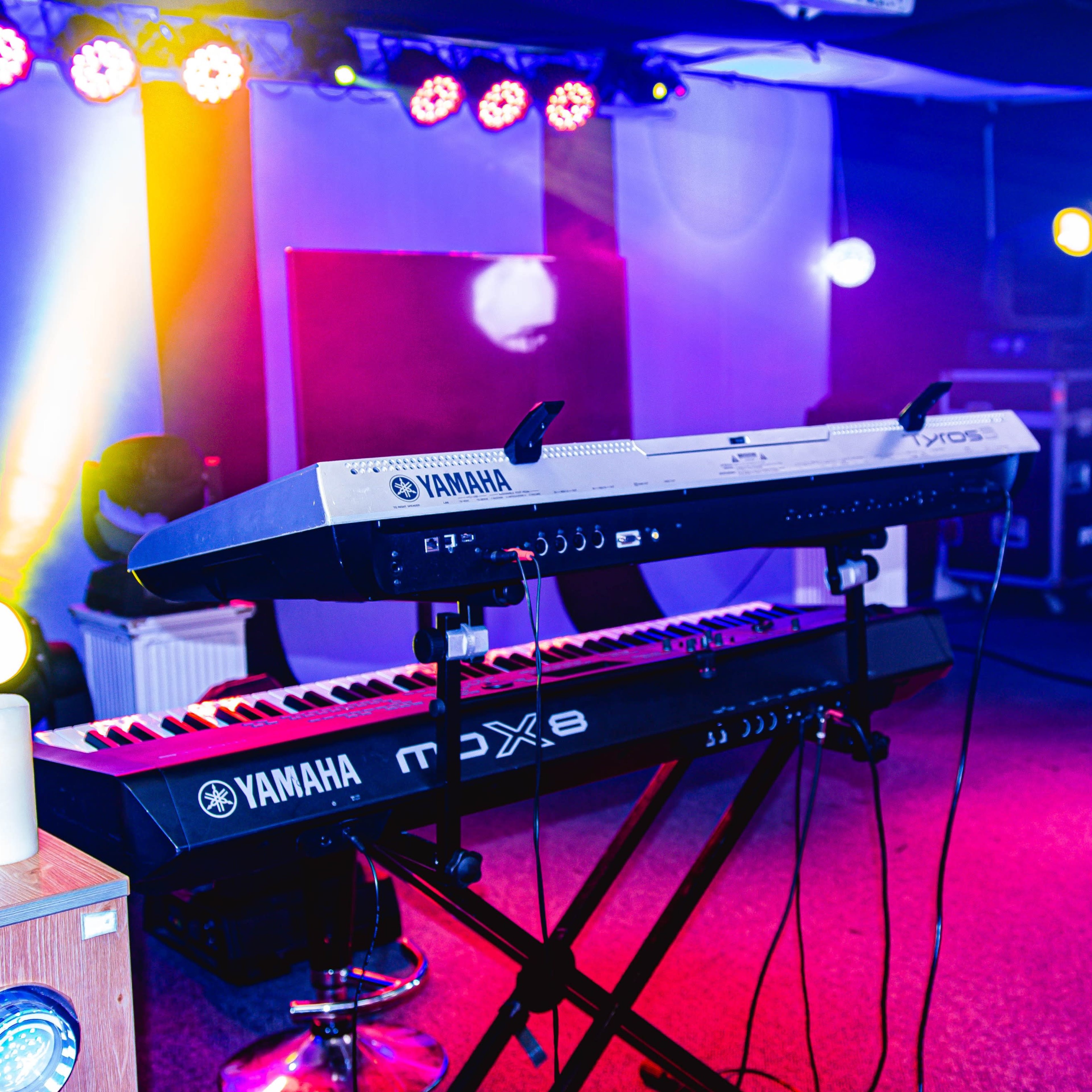 A music stage setup with two Yamaha keyboards illuminated by colorful stage lights.