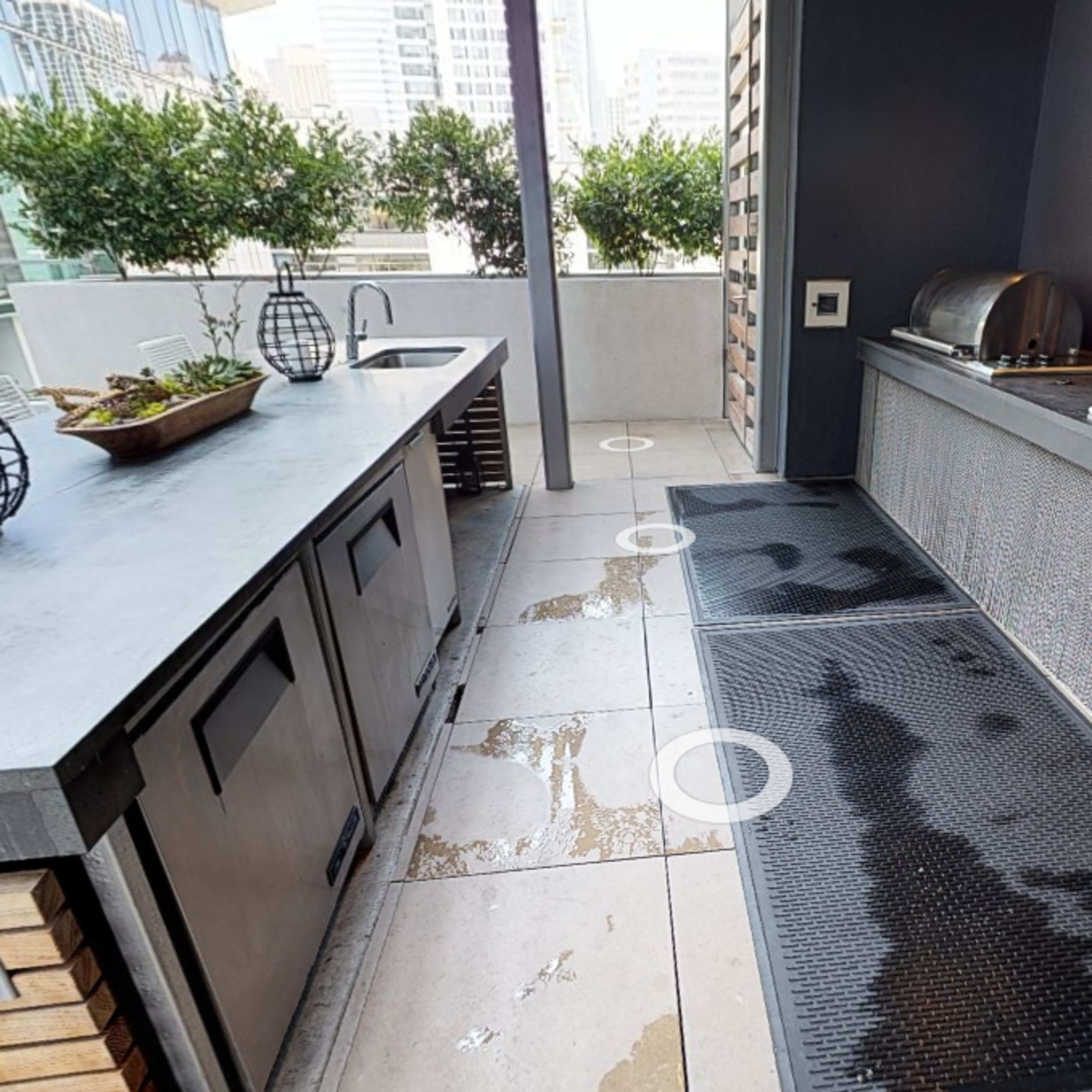 A modern outdoor kitchen area with a sink, grill, and tiled flooring surrounded by city buildings.