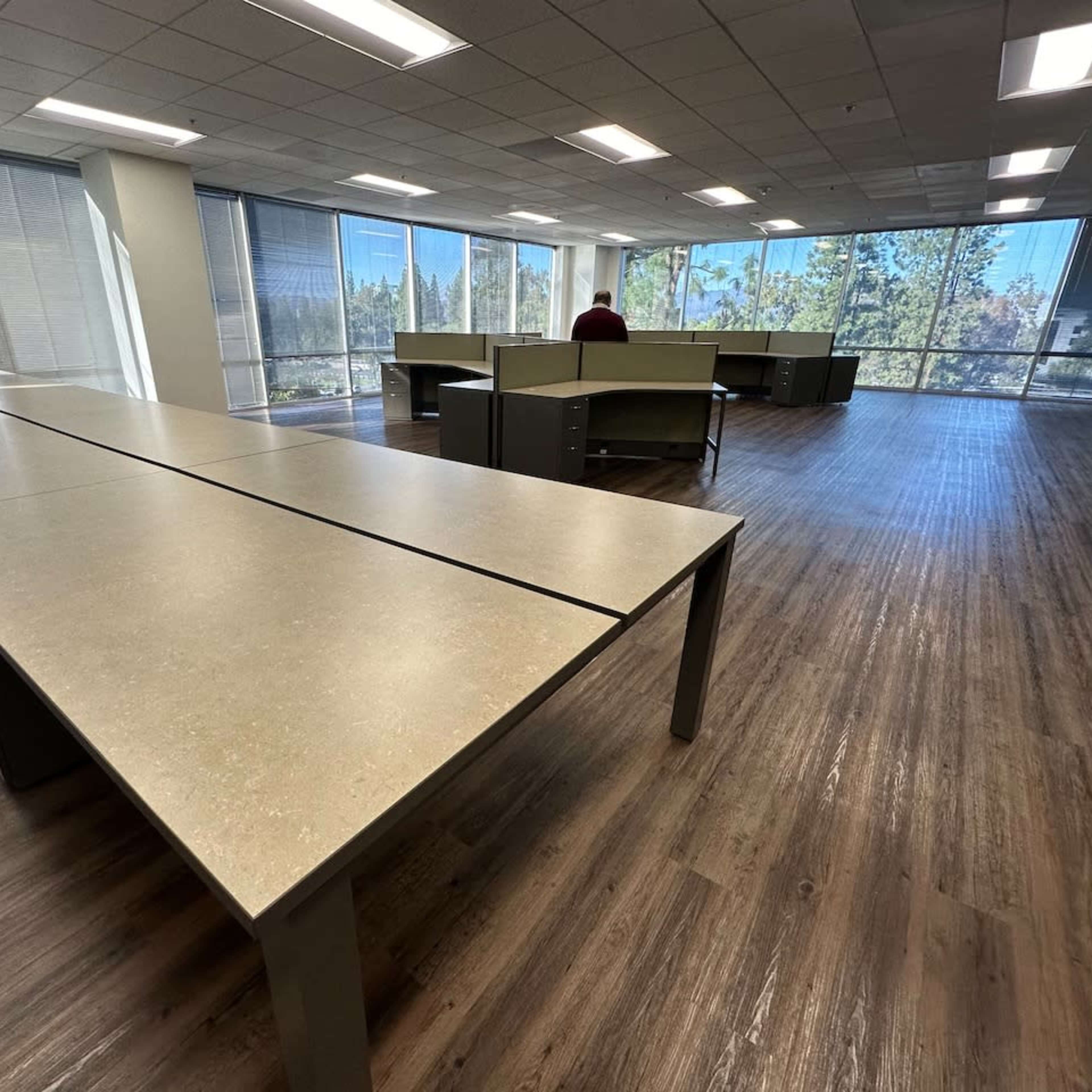 A spacious, modern office interior with large tables arranged in an open layout and multiple windows allowing natural light to enter.