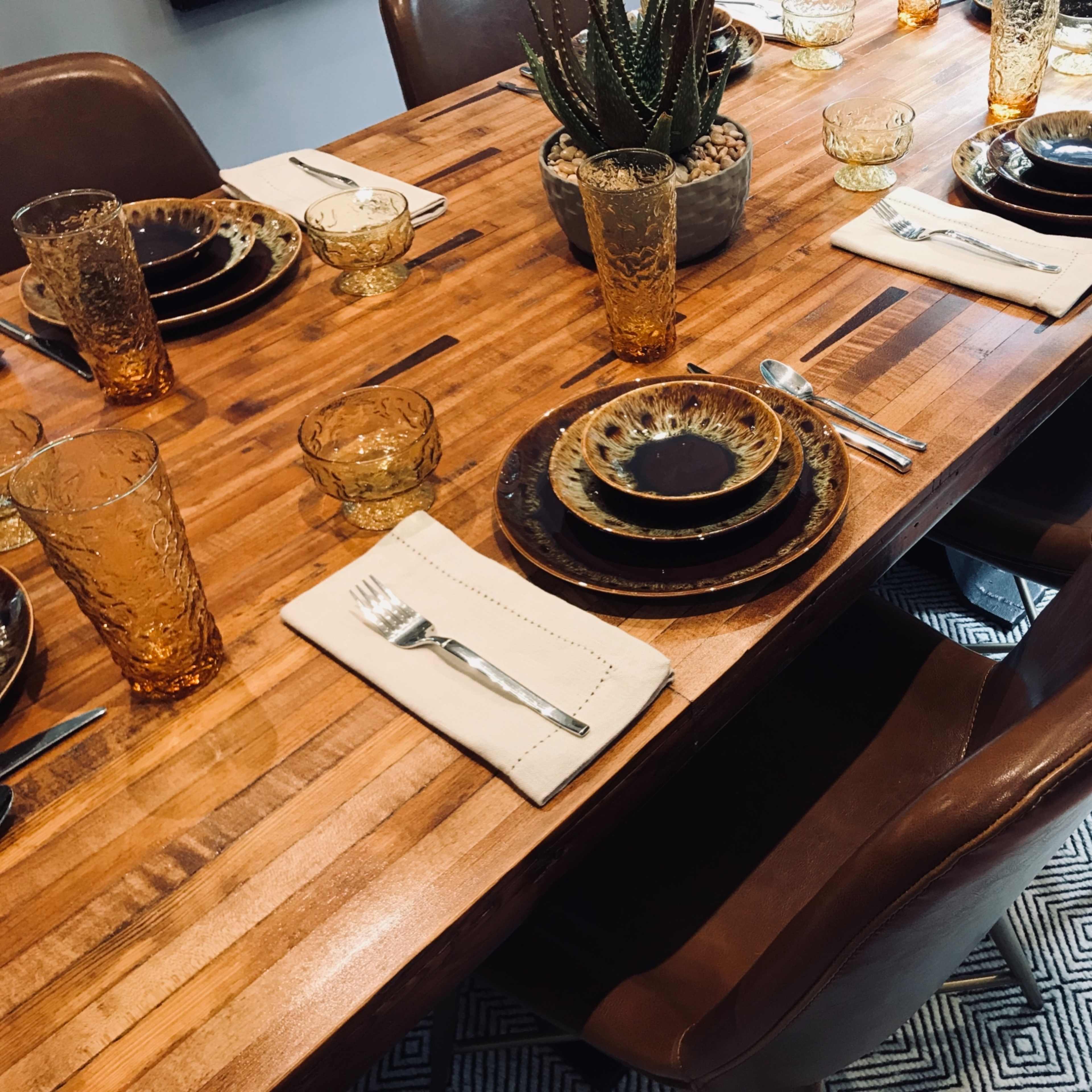A wooden dining table set with amber glassware, patterned plates, and cloth napkins, with leather chairs around it.
