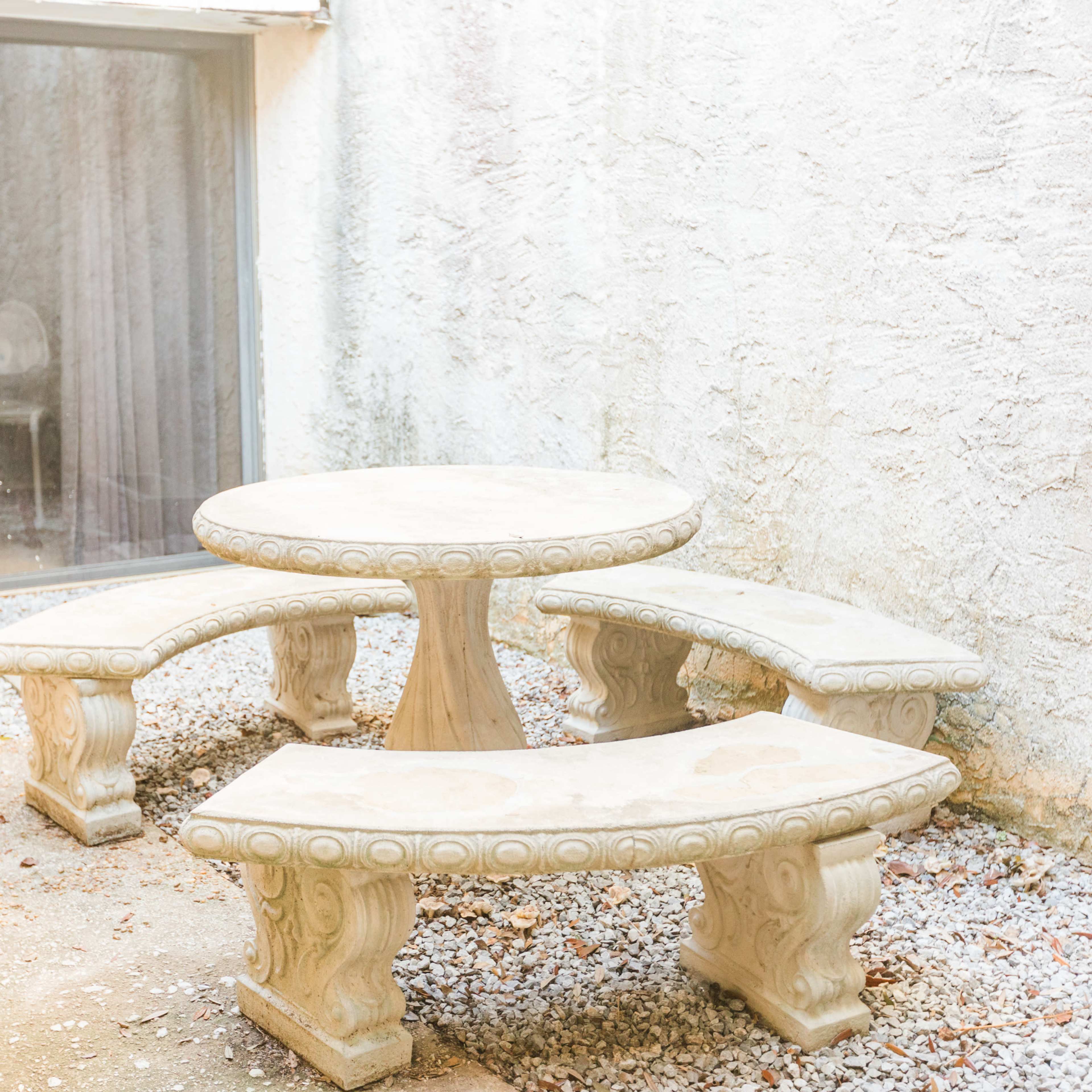 A circular stone table is surrounded by three matching curved benches in a gravel courtyard.