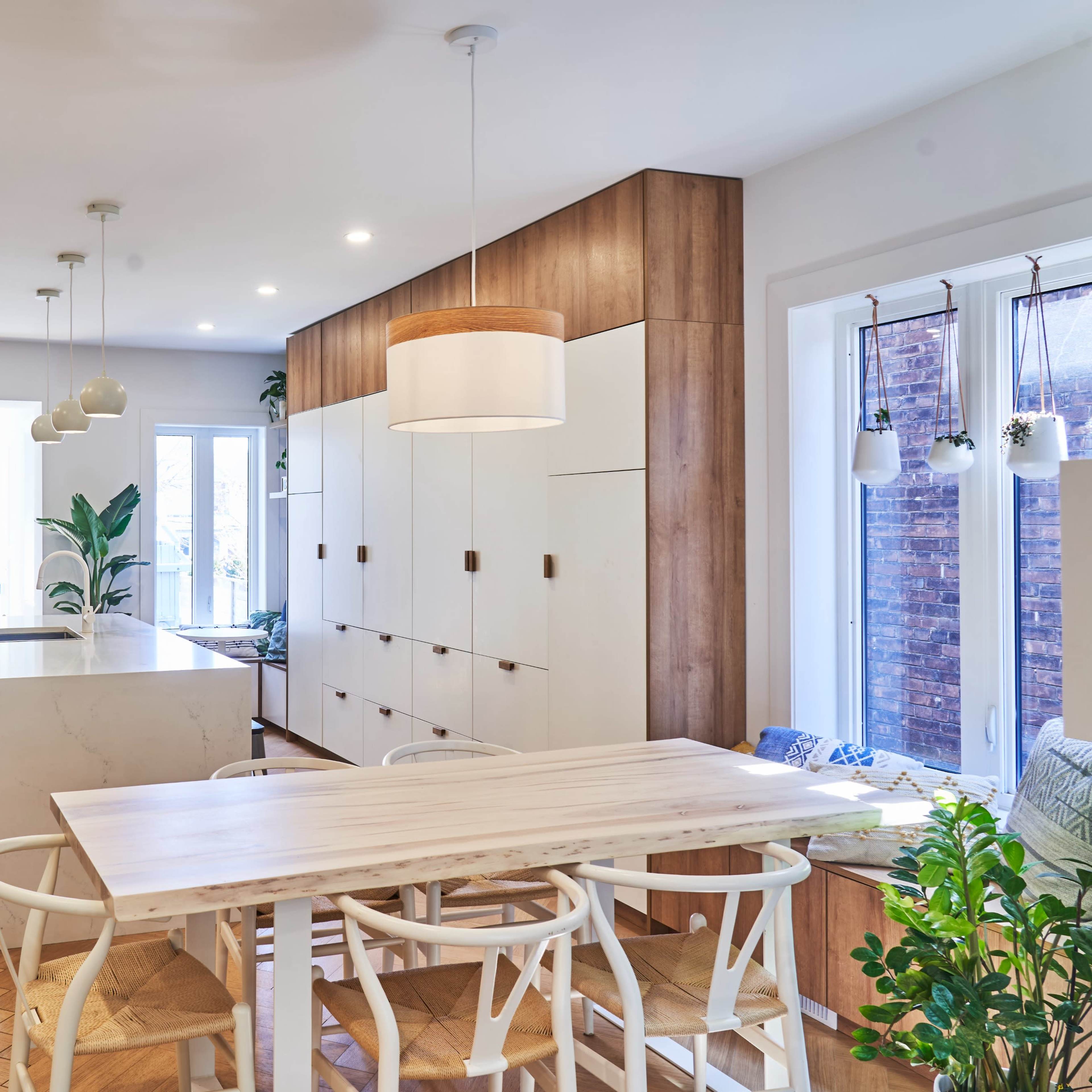 A modern kitchen and dining area with wooden cabinetry, a large white island, and a dining table surrounded by chairs, all illuminated by overhead lights.