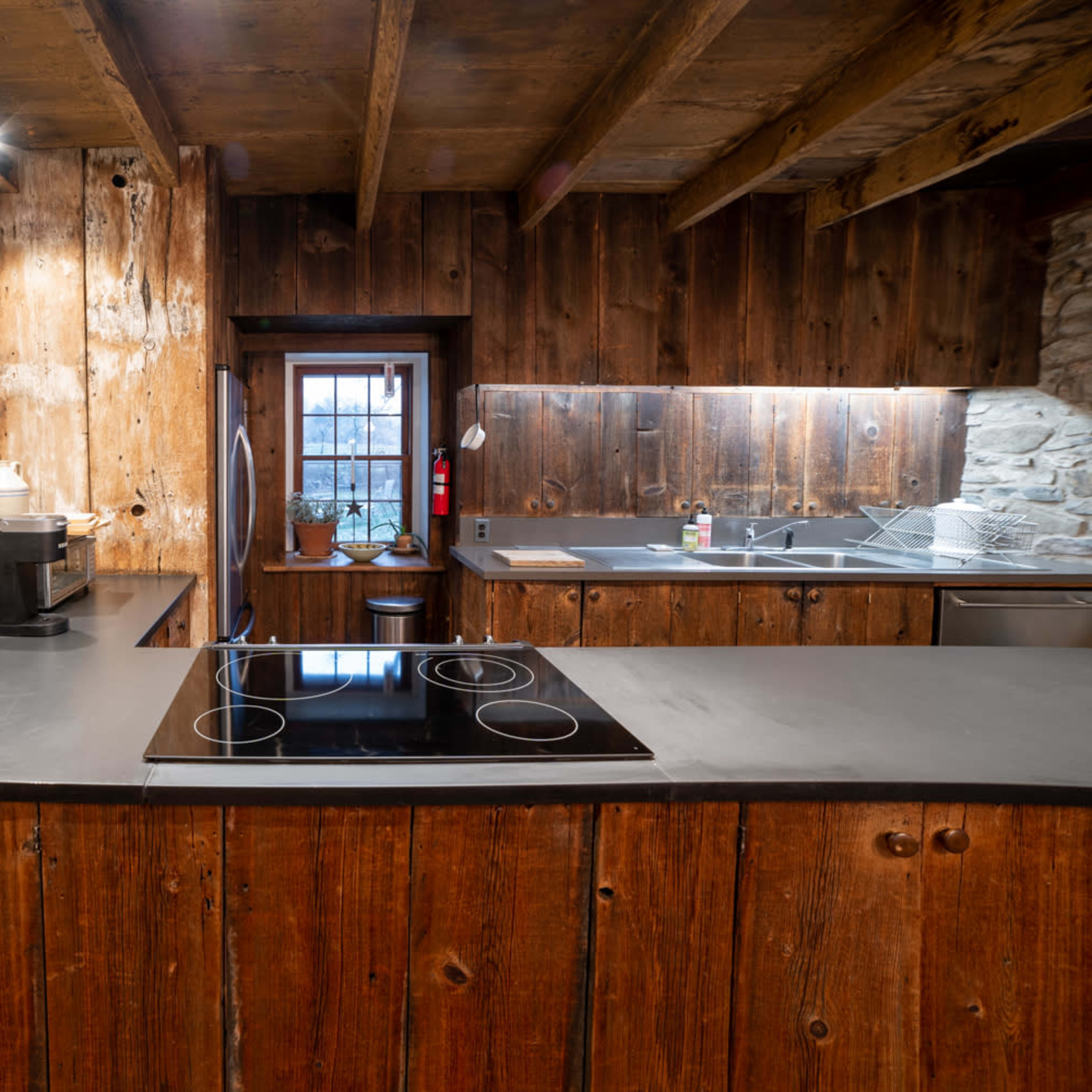 A rustic kitchen with stone and wooden walls, featuring a modern induction cooktop and an organized countertop.
