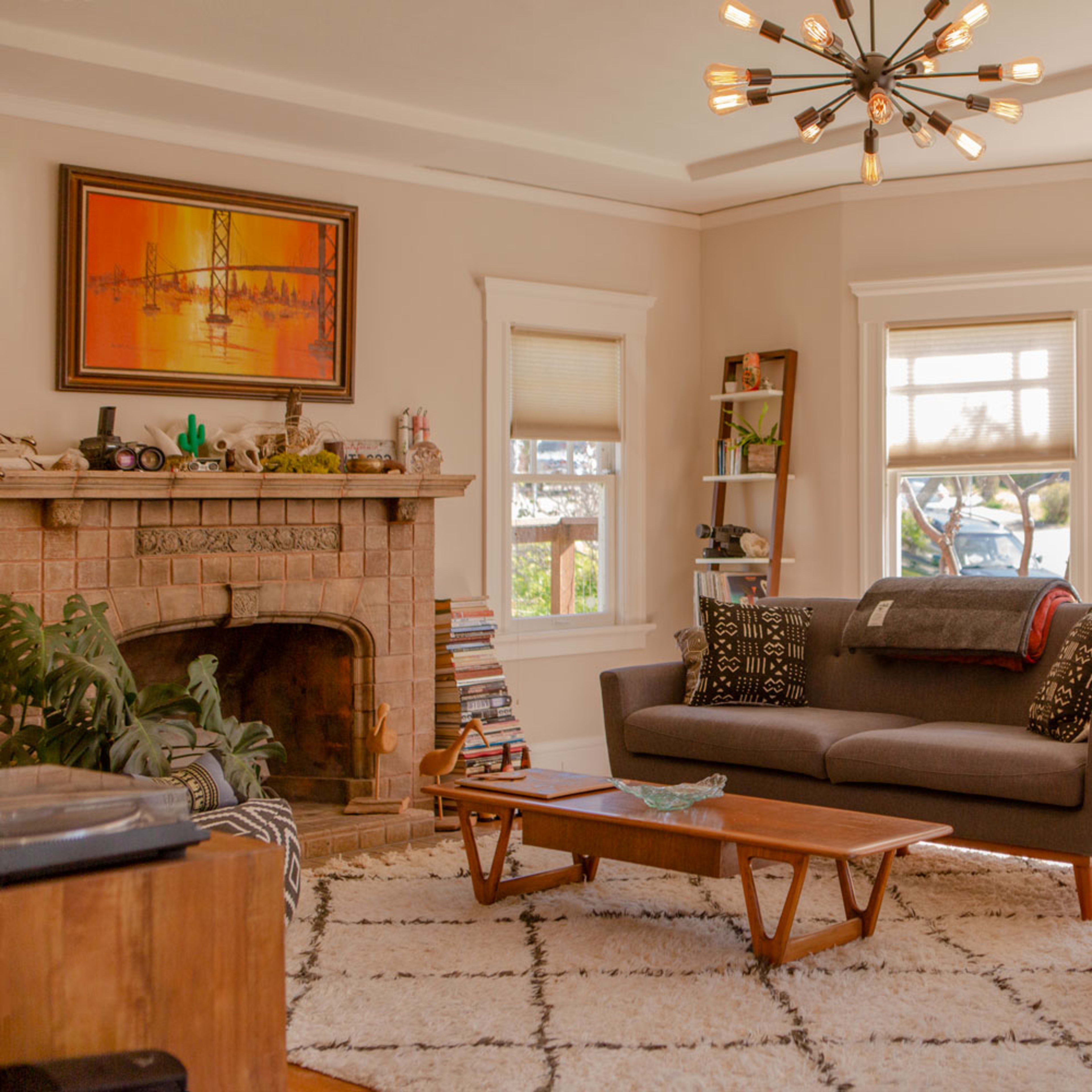 A cozy living room with a sectional sofa, a leather armchair, and a stone fireplace, complemented by large windows that let in natural light.