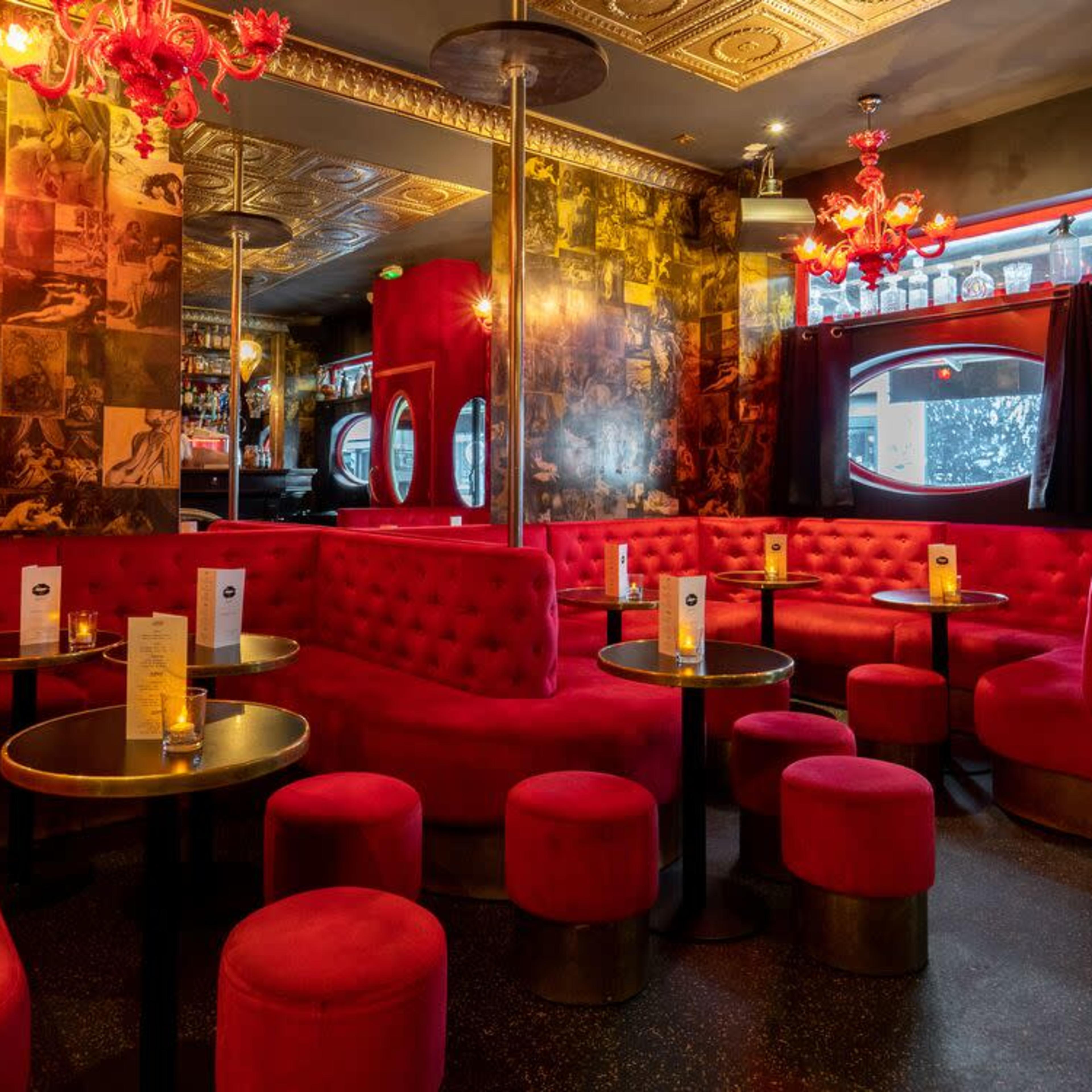 A vibrant lounge features red seating and decor, with round tables and dim lighting.