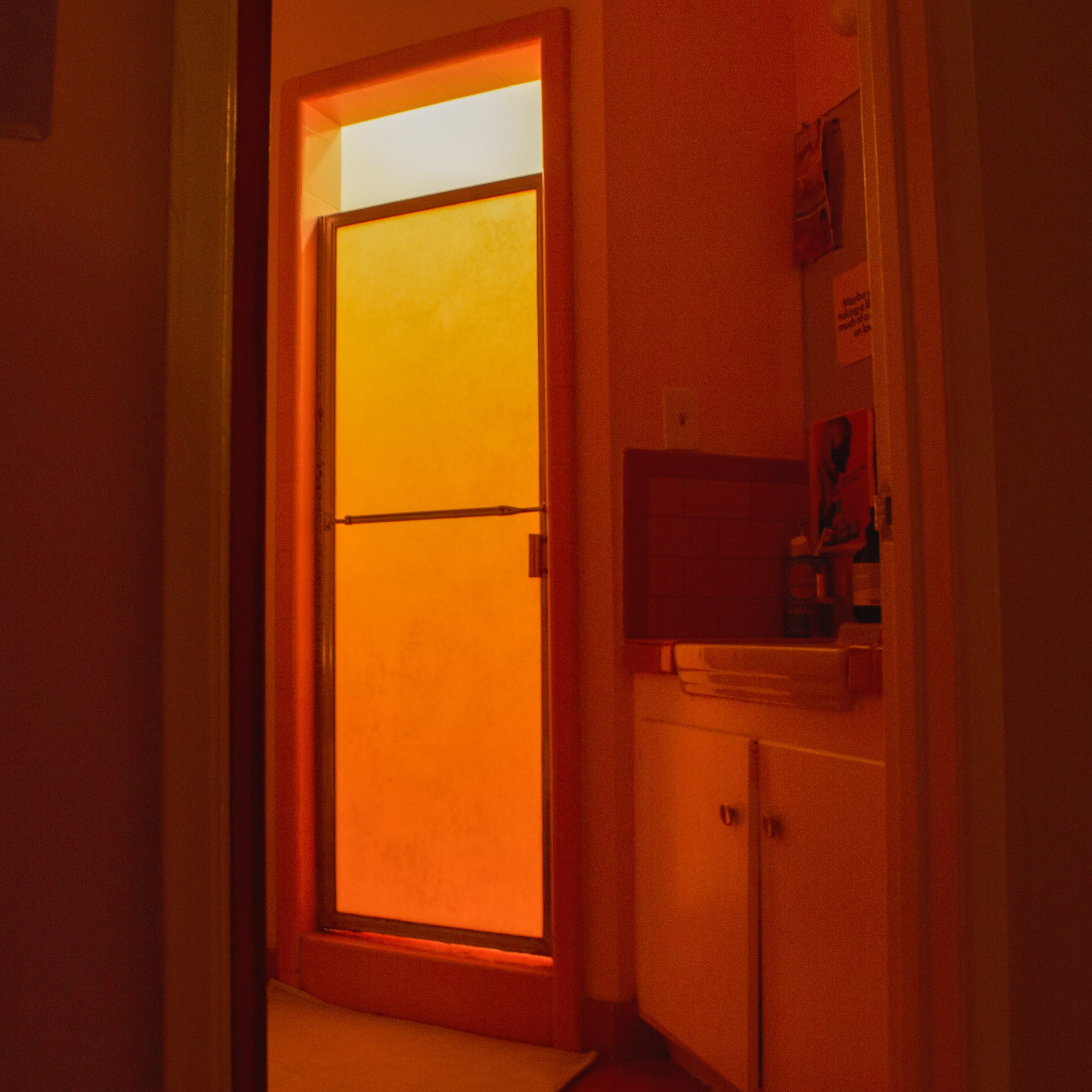 A brightly lit shower stall is visible through an open bathroom door, with a warm orange glow emanating from the interior.