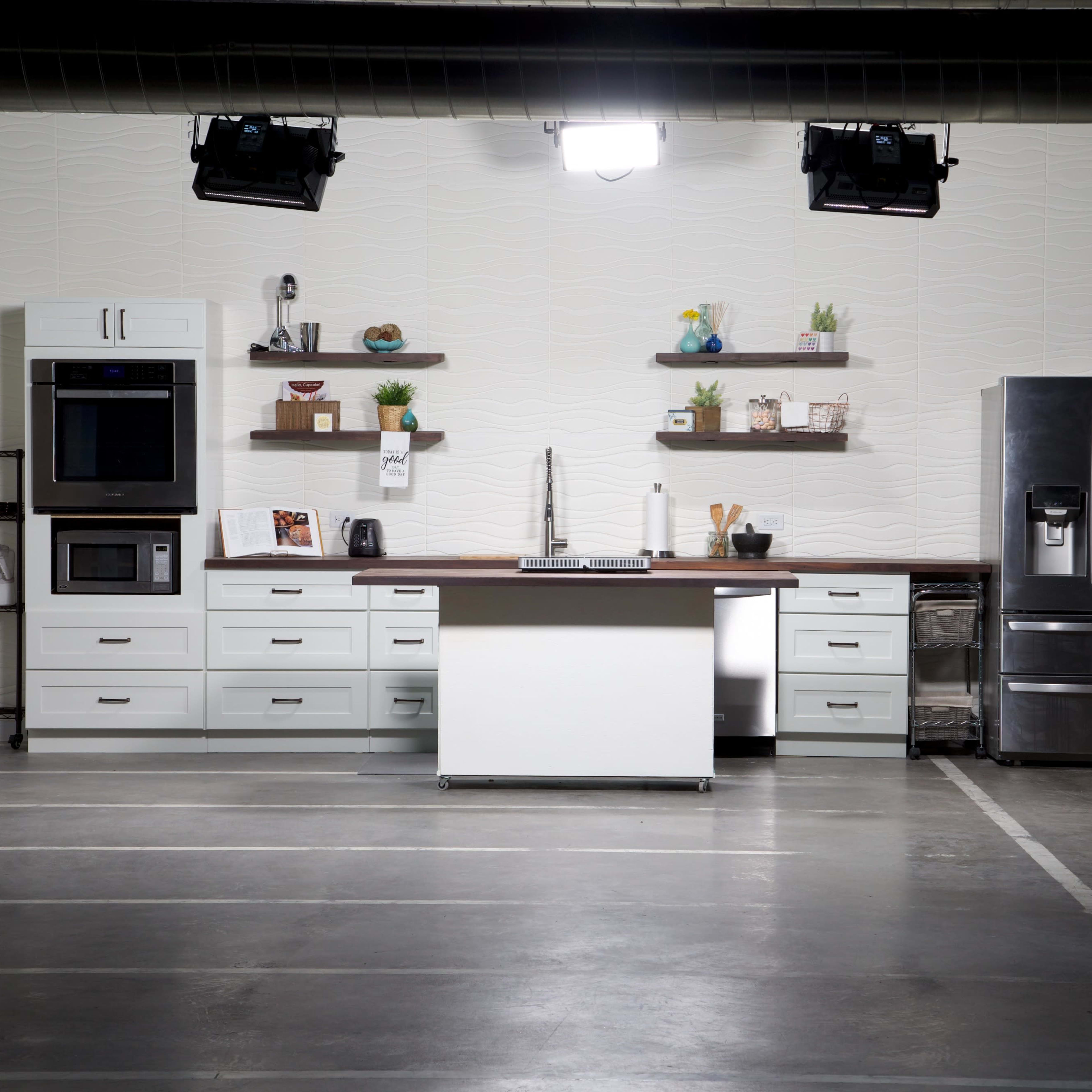 A modern kitchen setup with white cabinets, stainless steel appliances, and open shelves displaying decorative items.