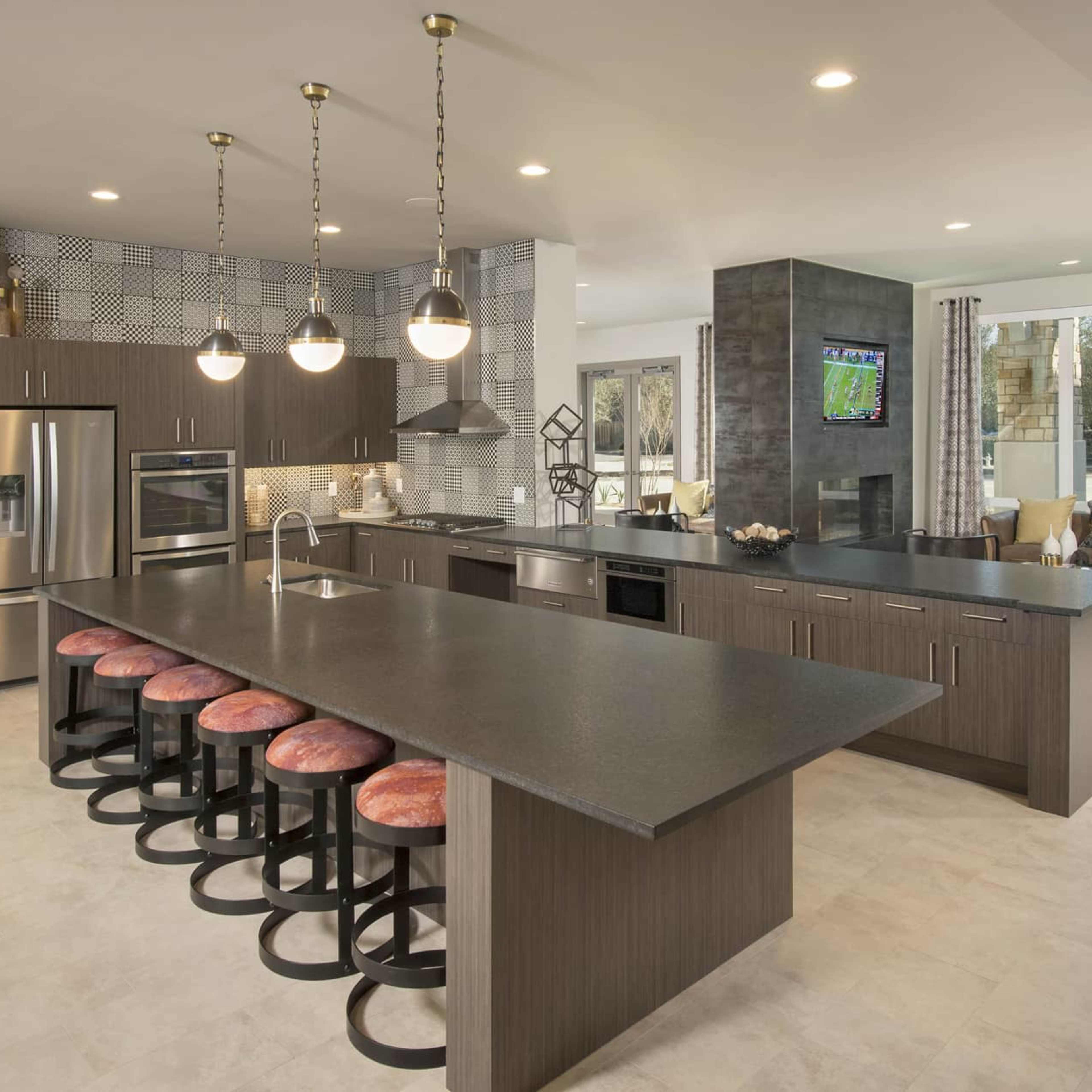 A spacious modern living area with a lounge featuring a sofa and coffee table, a dining area with blue chairs, and a kitchen visible in the background.