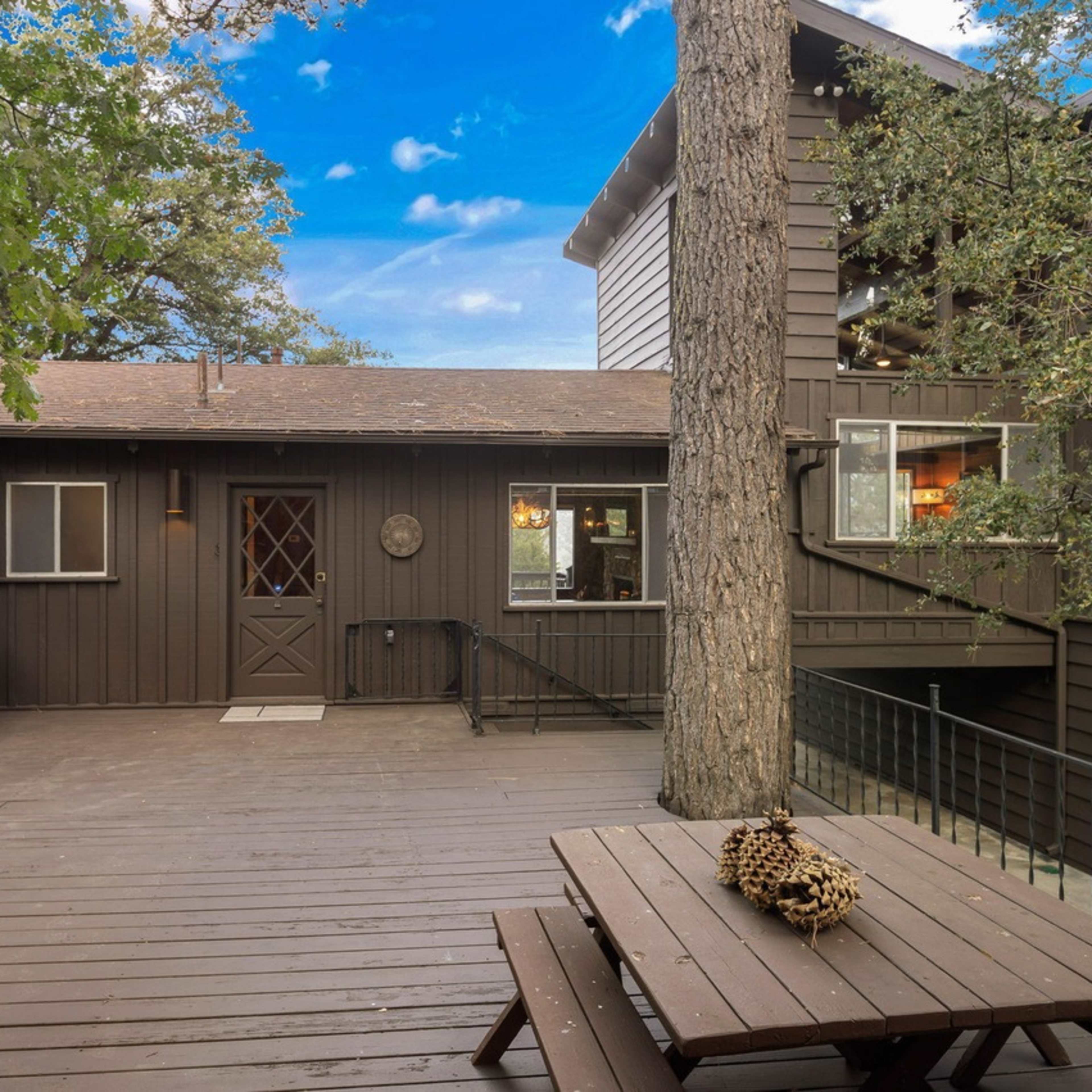 A wooden deck area of a dark-colored house surrounded by trees, featuring a grill and a picnic table.