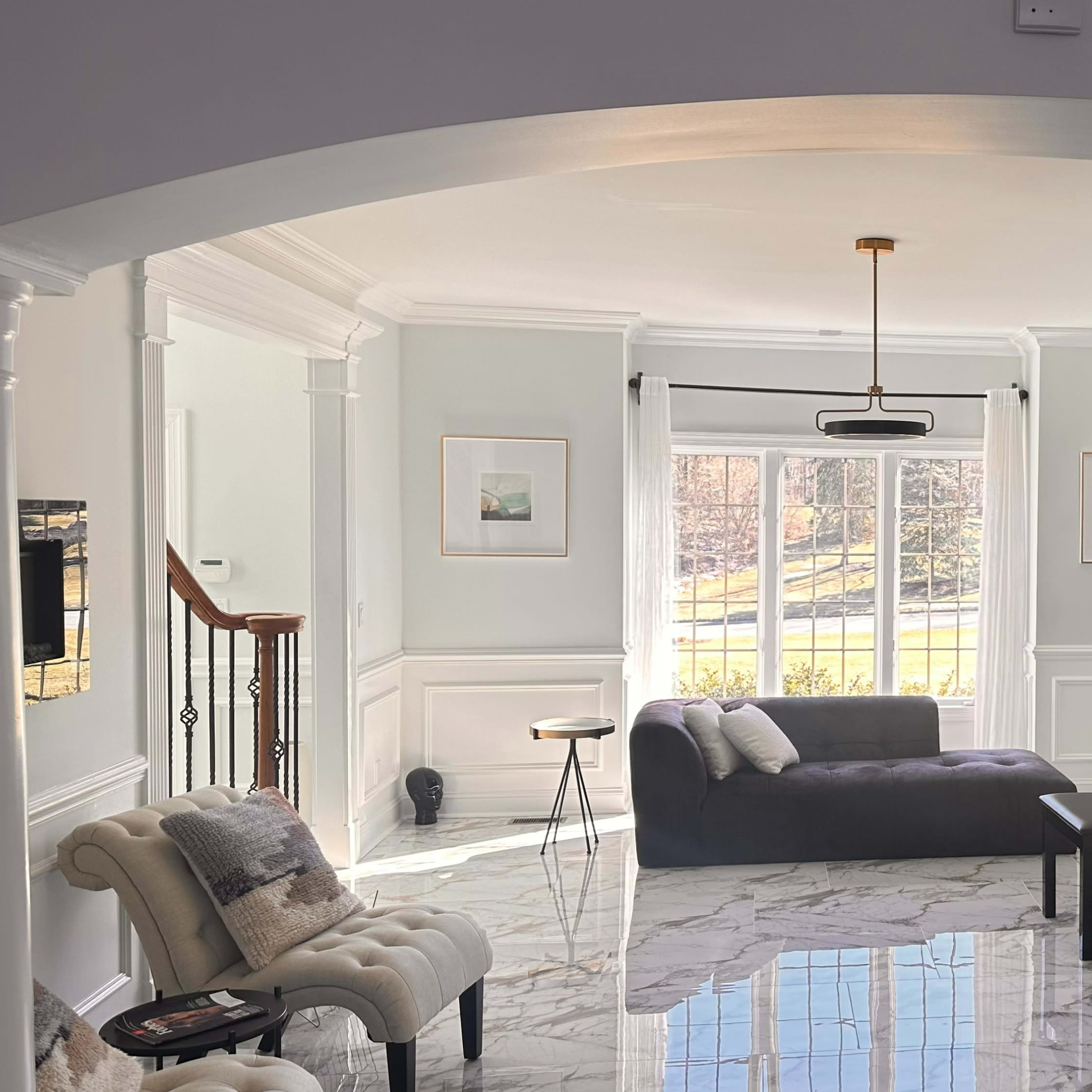A bright living room featuring a black piano, a gray sofa, and marble flooring with large windows that allow natural light to enter.