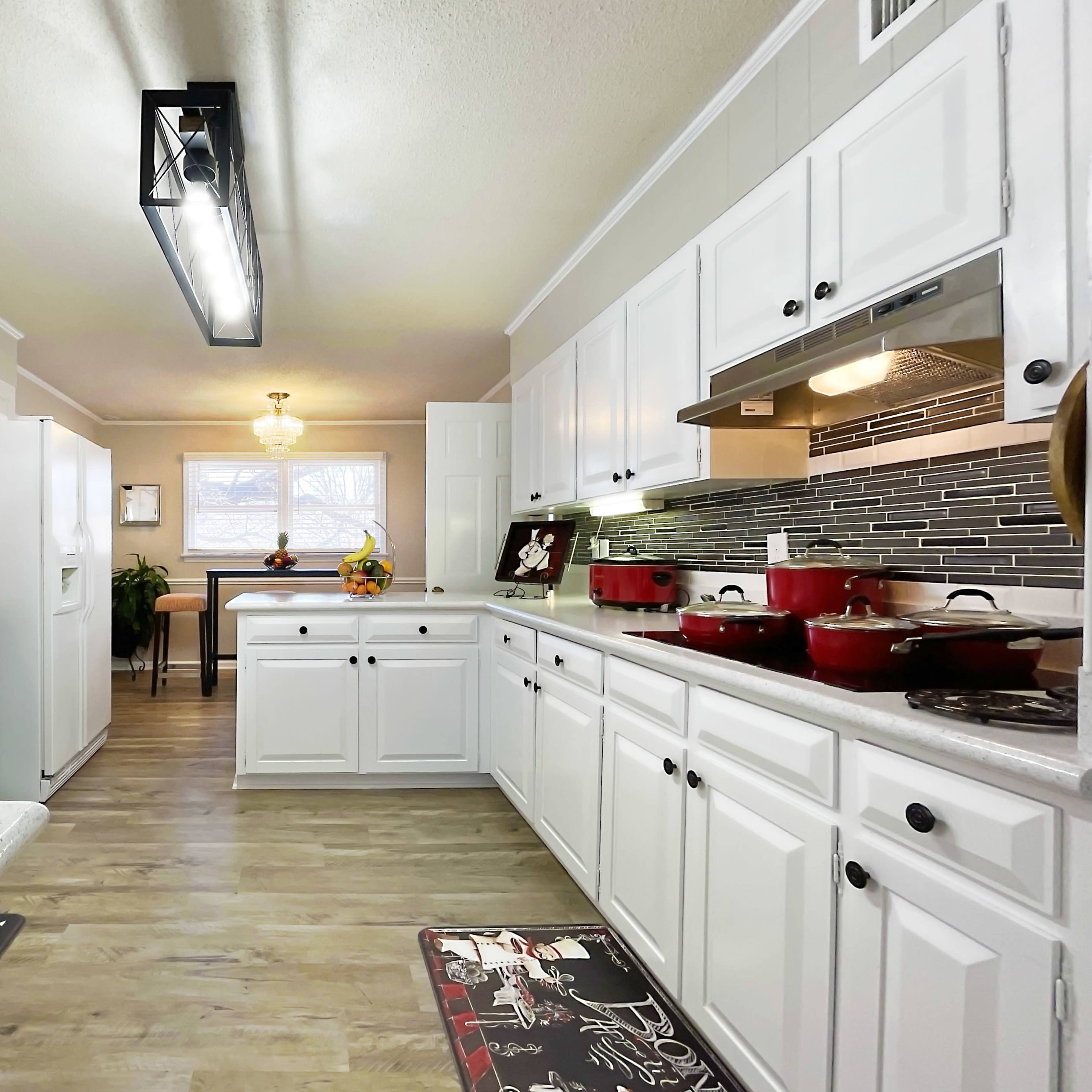 A bright kitchen with white cabinets, stainless steel appliances, and a central island featuring a sink, along with red cookware on the countertops.