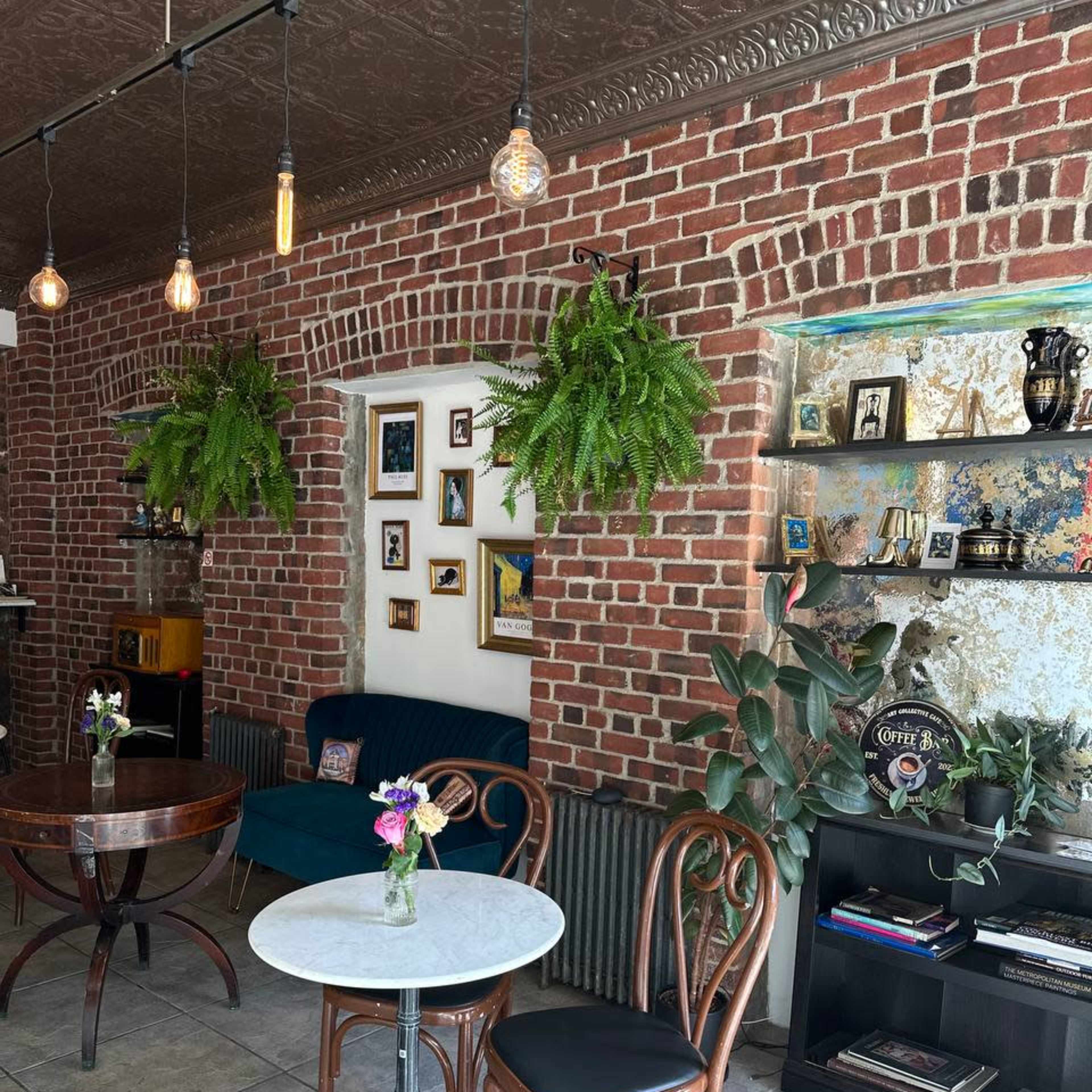 A cozy café interior with exposed brick walls, hanging plants, and a mix of furniture including a round marble table and wooden chairs.