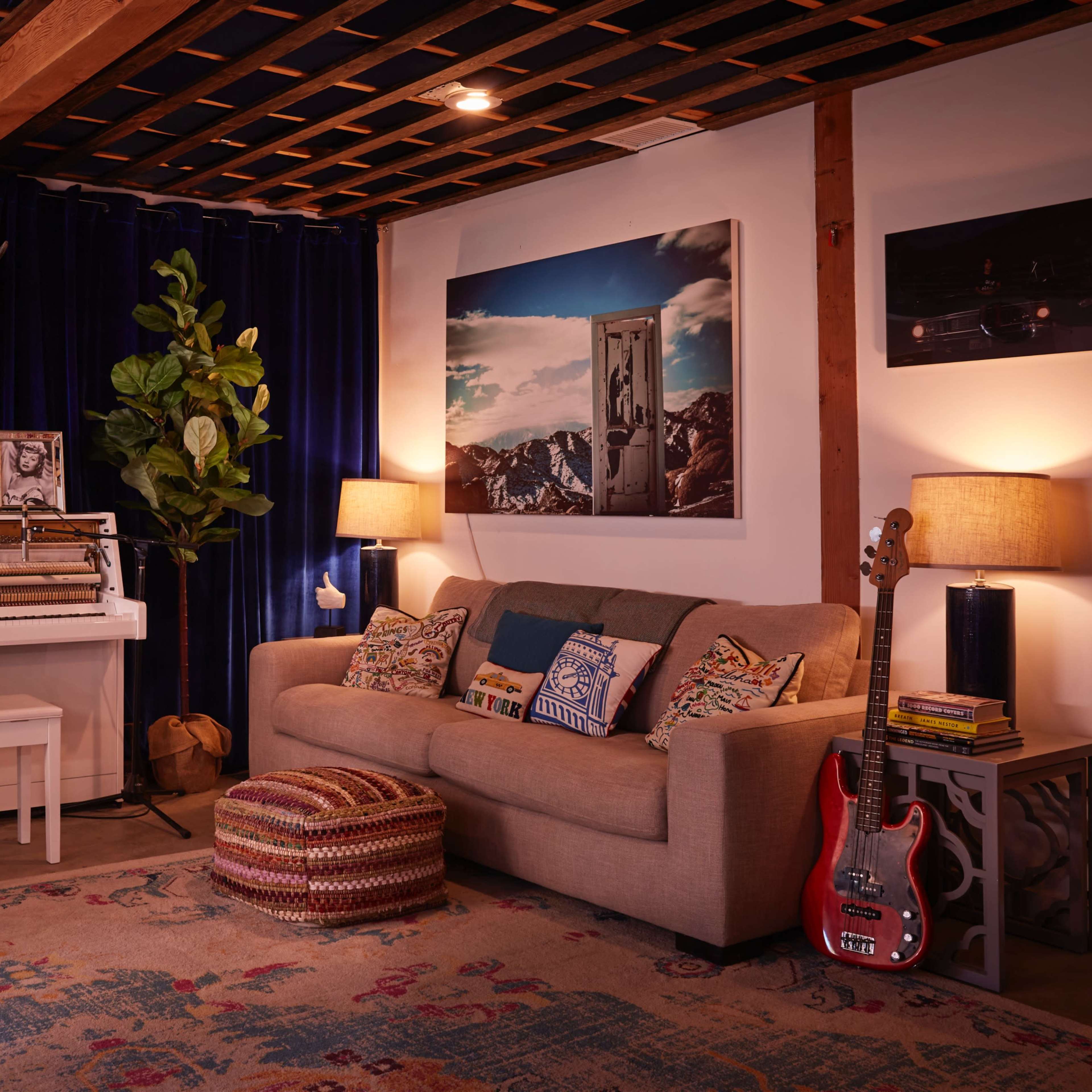 A cozy music room features a piano, guitars, a comfortable sofa, and decorative elements against a backdrop of blue curtains and wooden beams.