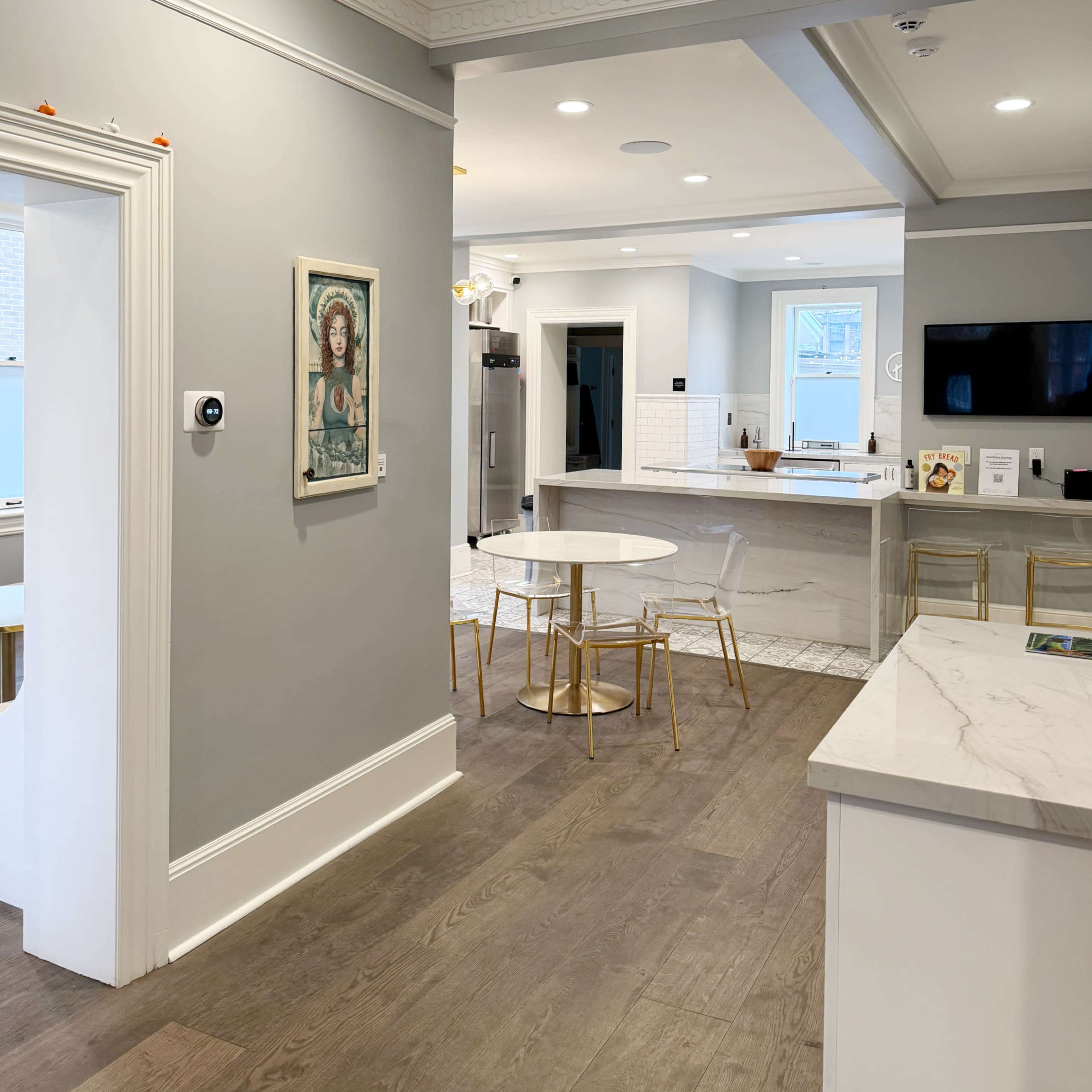 A modern kitchen and dining area with light gray walls, a marble countertop, and a small round dining table with gold-accented chairs.
