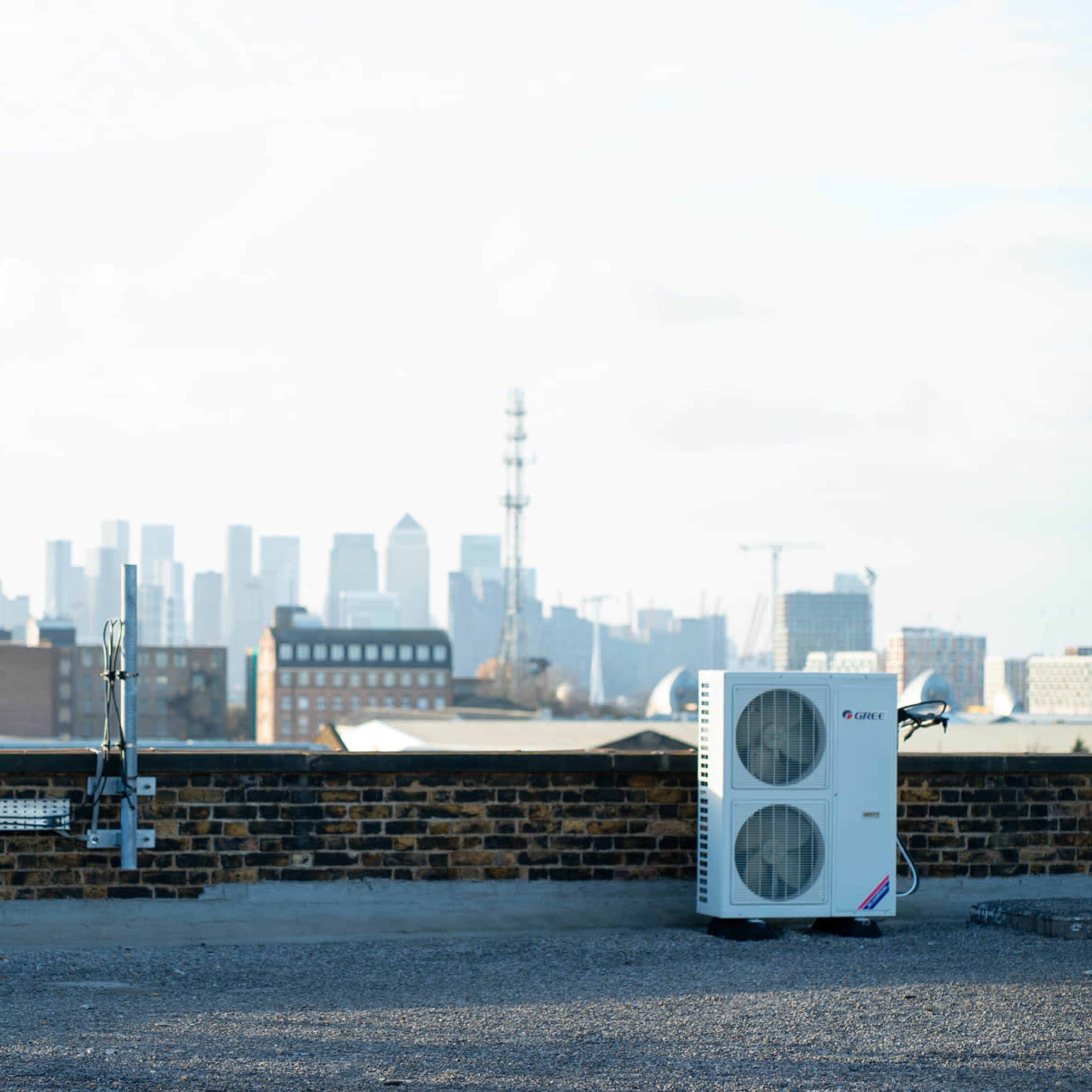 A rooftop with an air conditioning unit on one side and a view of a city skyline in the background.